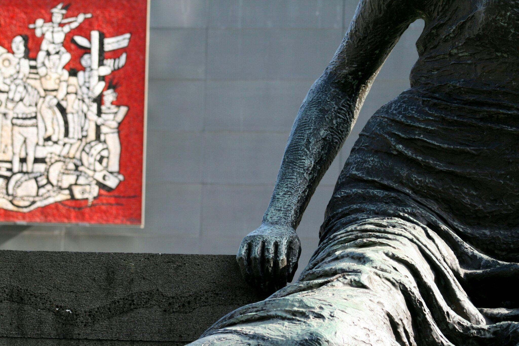 Detalle de una estatua de bronce con inscripciones asiáticas sobre un panel rojo al fondo