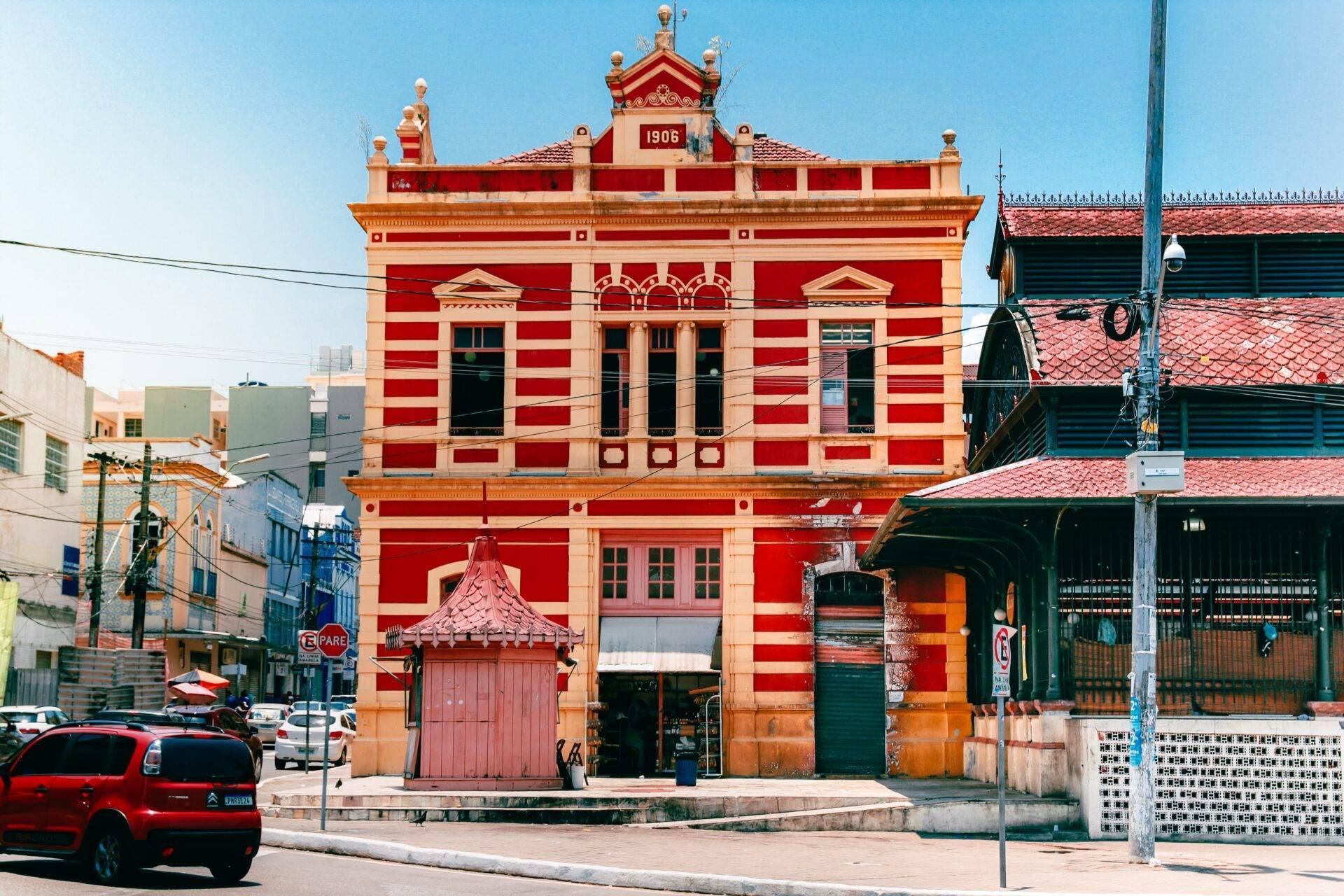 Historisches rot-weißes Gebäude aus dem Jahr 1906 im Kolonialstil, umgeben von modernen Stadtstraßen