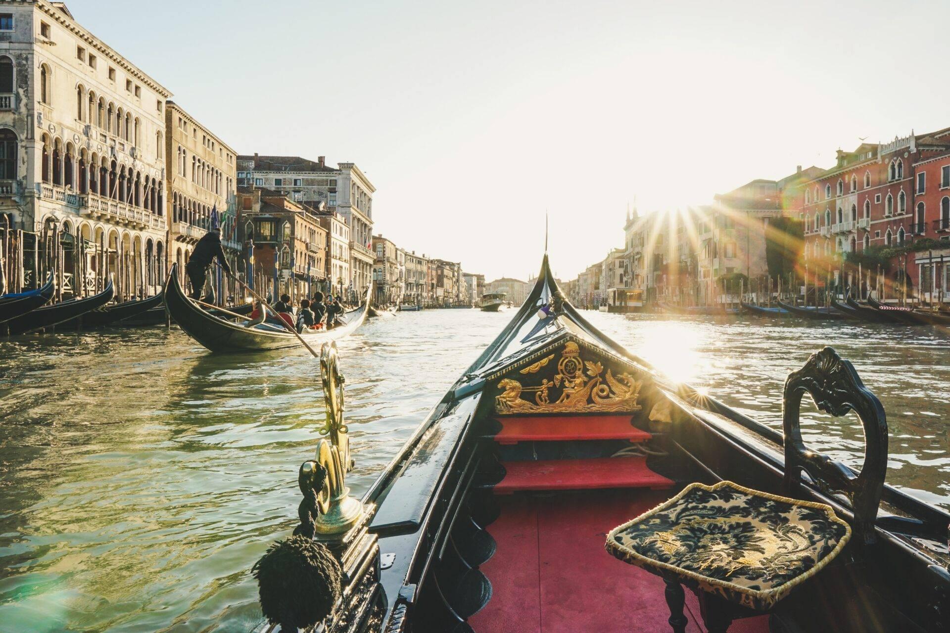 Vista da una gondola veneziana decorata che naviga sul Canal Grande con palazzi storici e luce solare