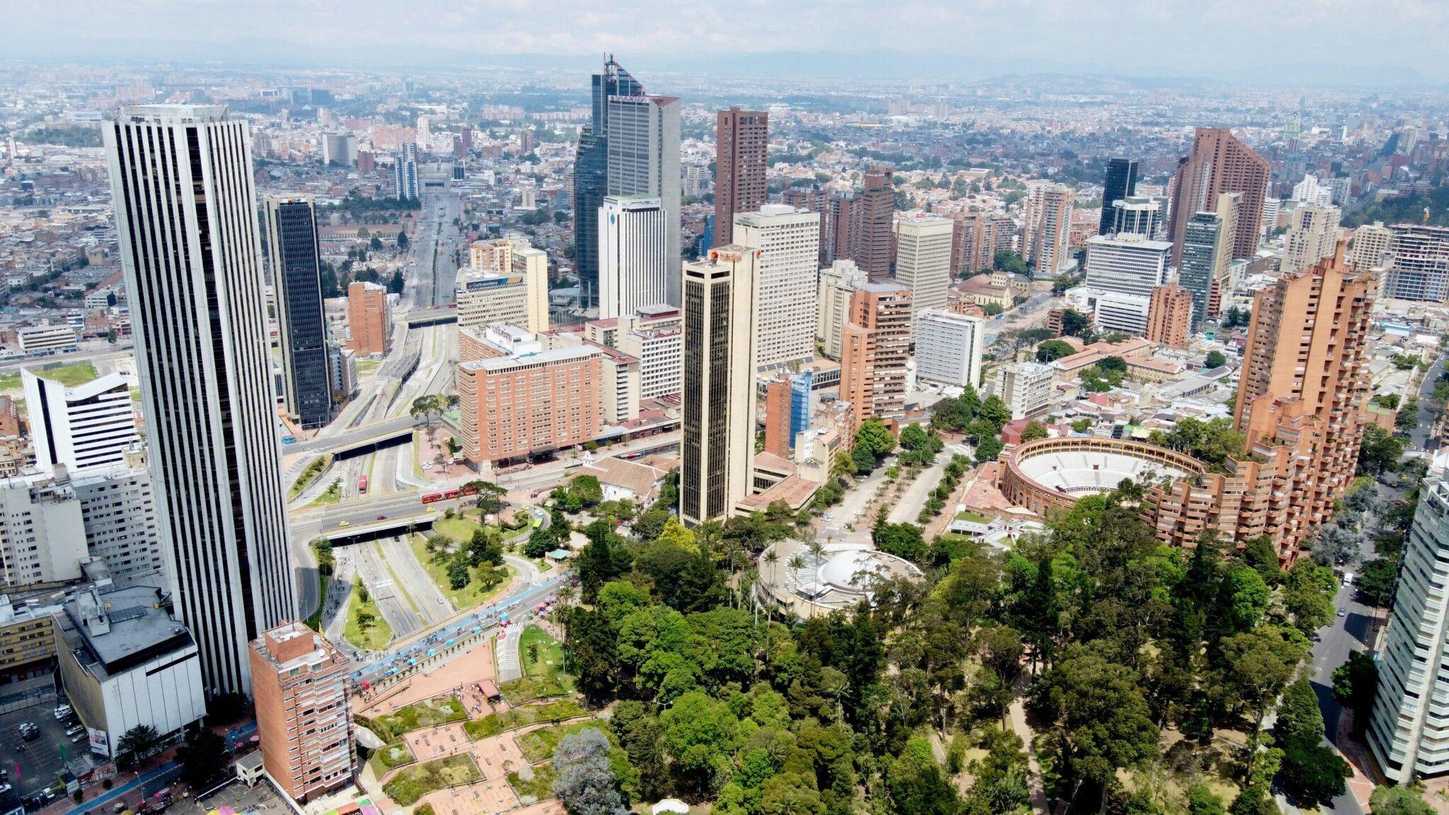 Vista aérea de una gran ciudad andina con rascacielos, edificios de colores, zonas verdes y montañas al fondo