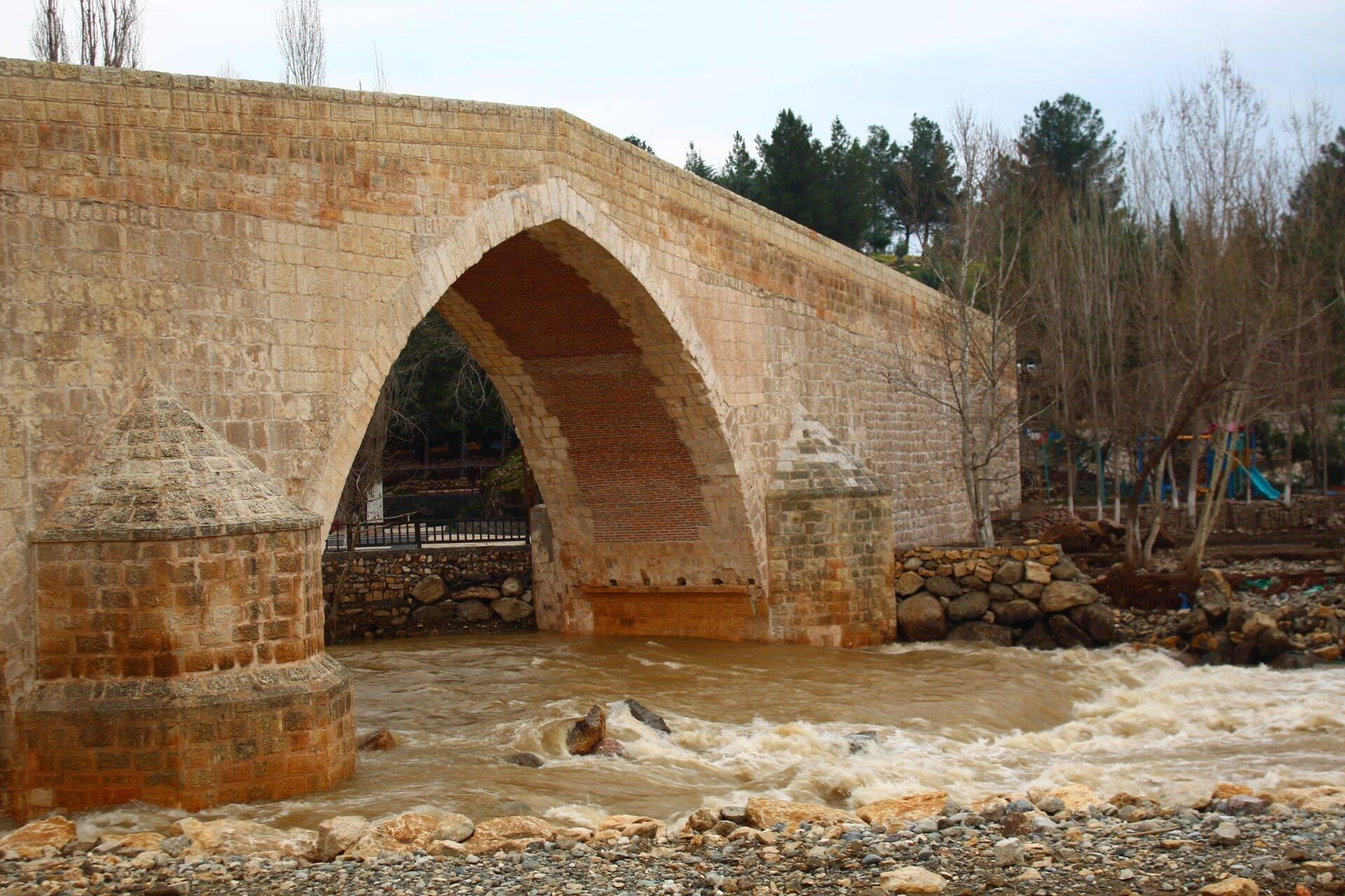 Eine alte Steinbrücke mit einem großen Bogen überspannt einen reißenden trüben Fluss