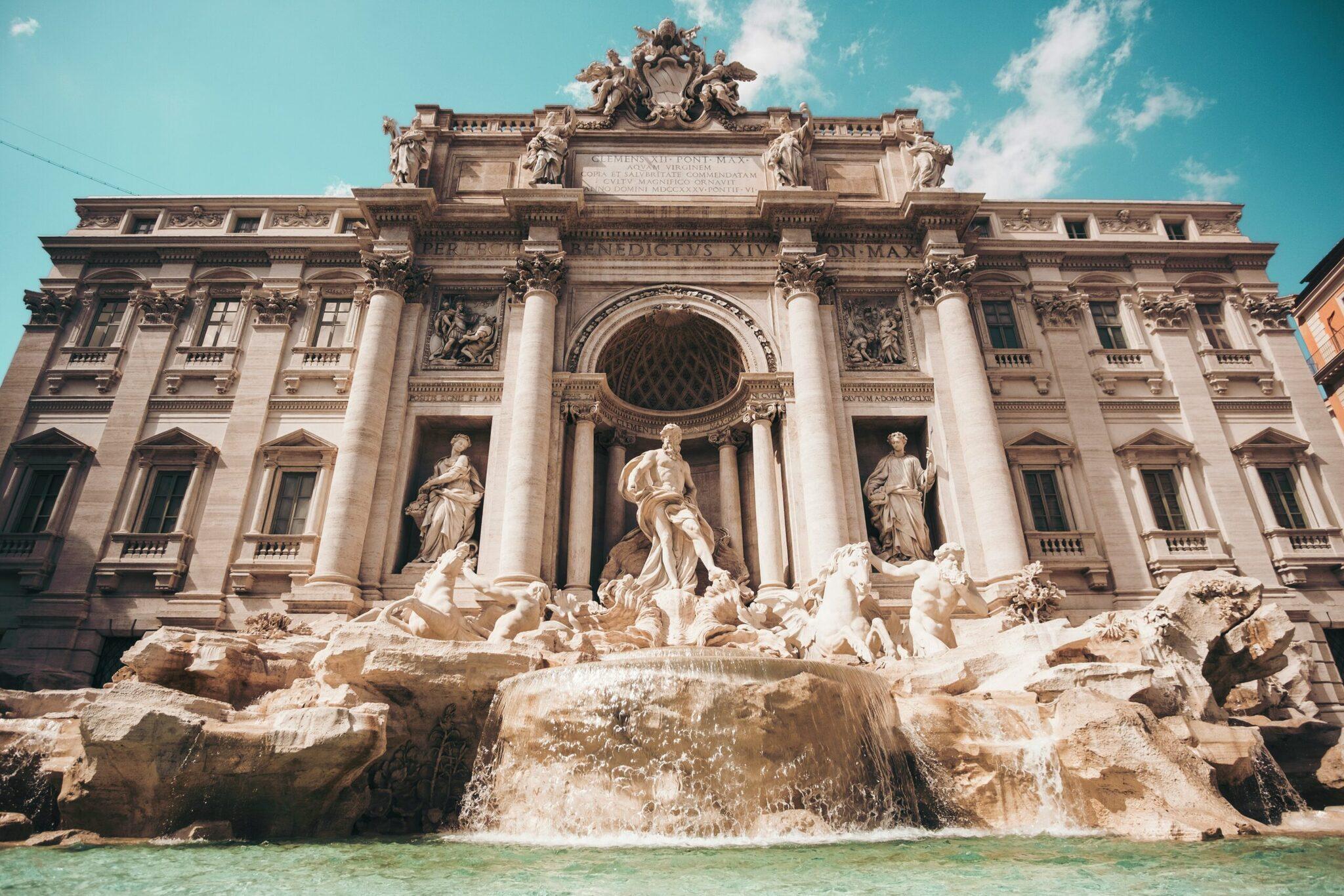 La Fontana di Trevi con su majestuoso edificio barroco, sus esculturas y su estanque de agua turquesa bajo un cielo despejado
