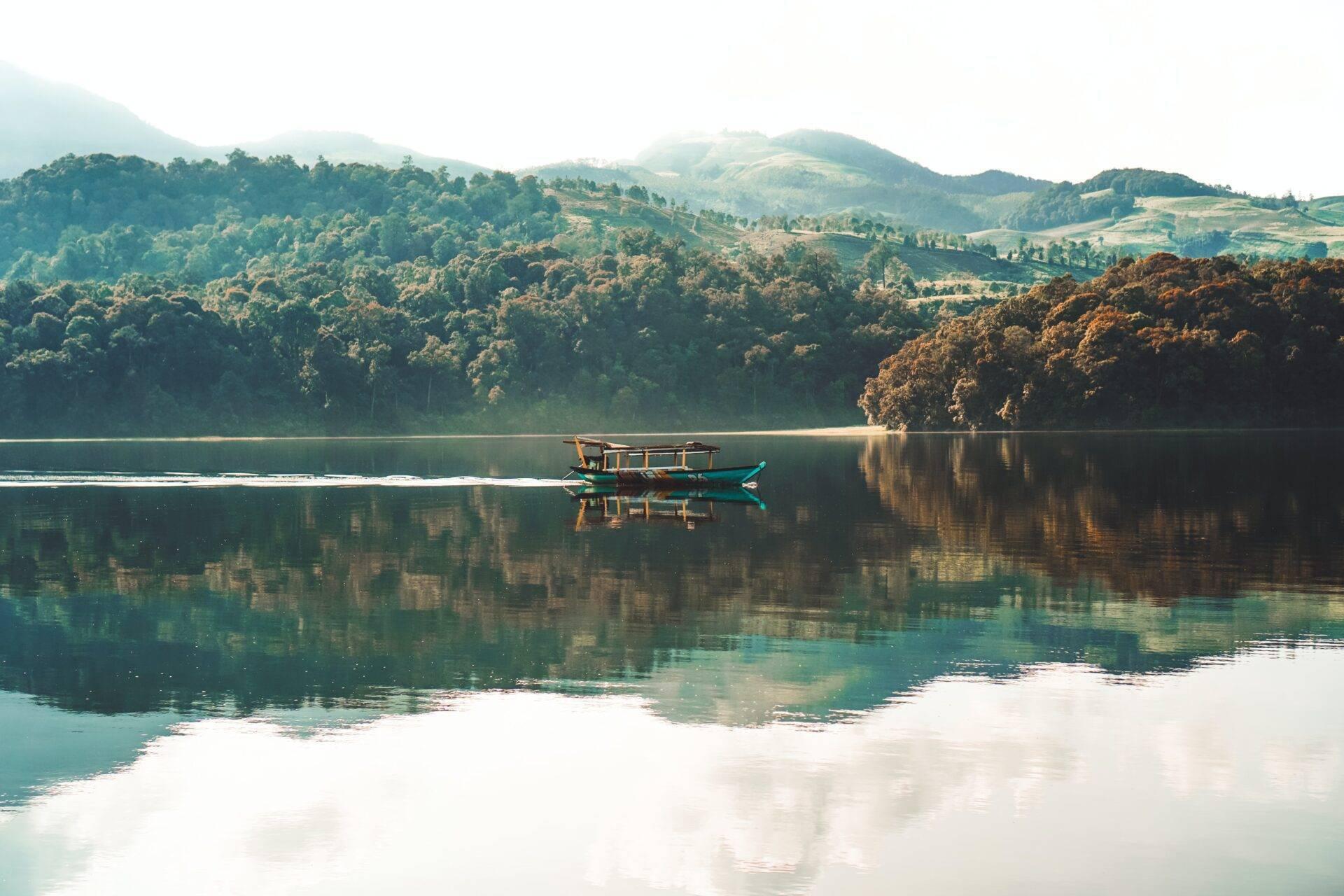 Una barca da pesca tradizionale blu su un lago specchio circondato da montagne boscose e giungla verdeggiante