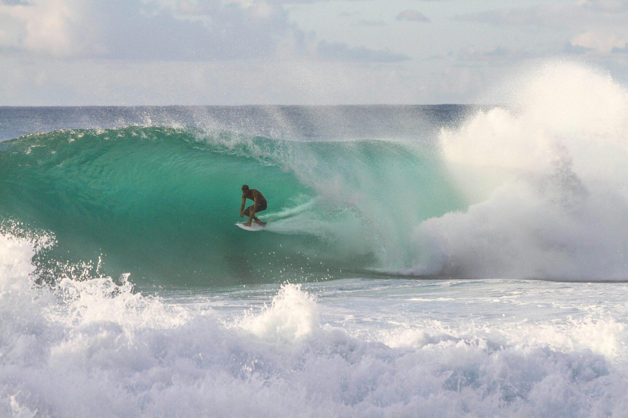 A surfer riding a hollow turquoise wave on a sunny ocean beach