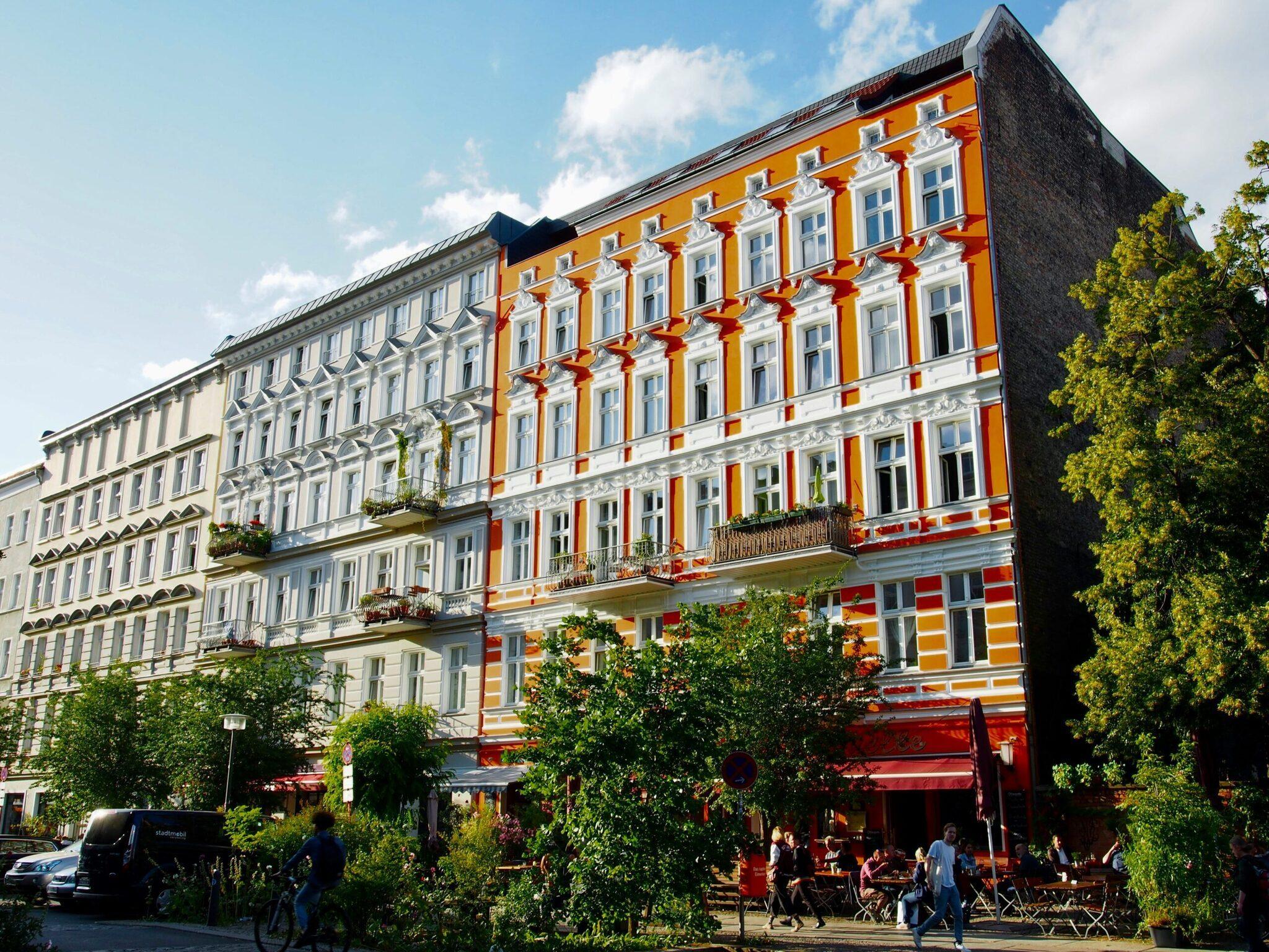Colorido edificio de estilo Gründerzeit con fachada naranja y roja, animada terraza en la planta baja y hiedra en los laterales