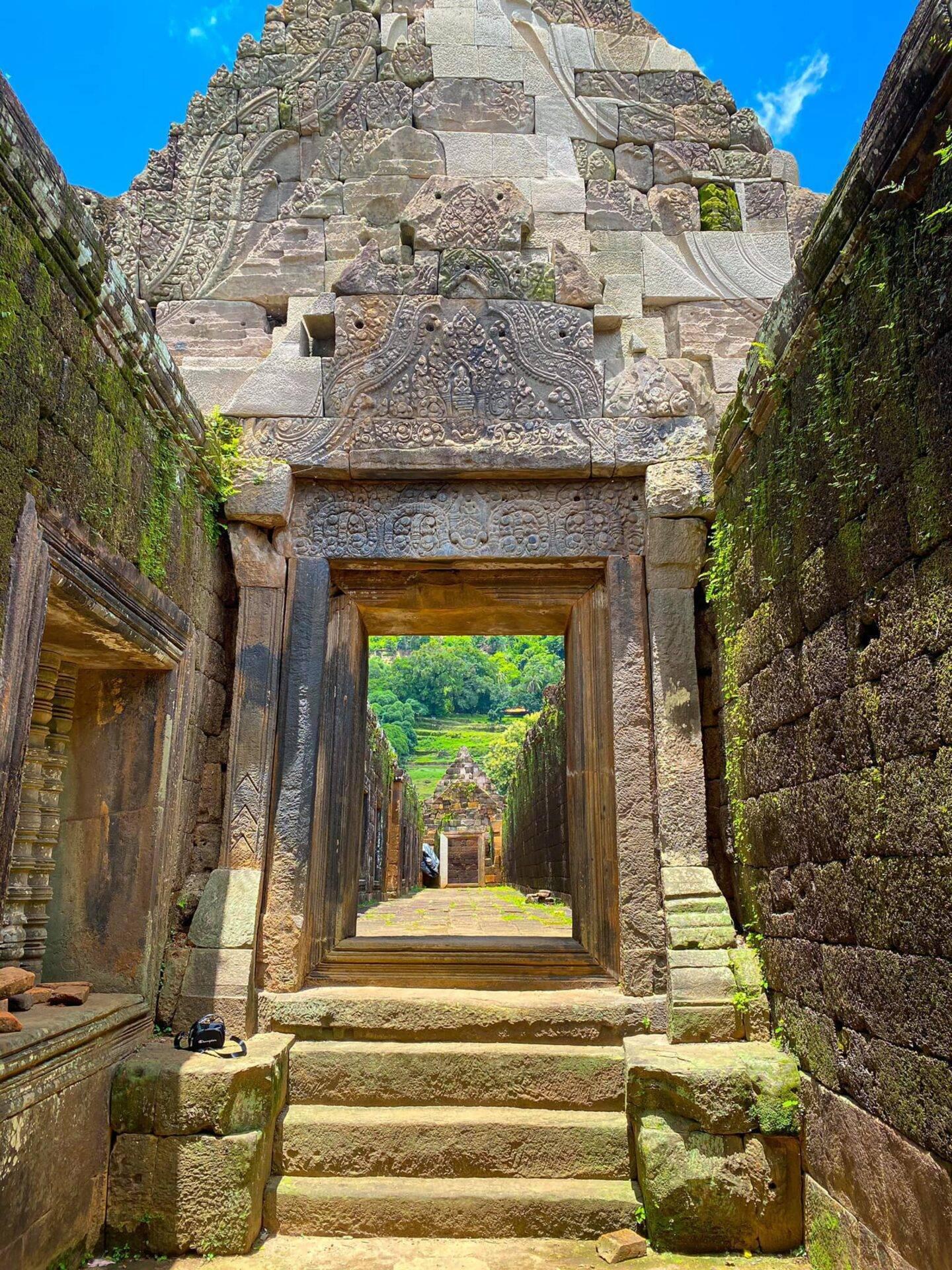 Enfilata di porte ornamentate di un antico tempio khmer, con giungla verdeggiante visibile in lontananza