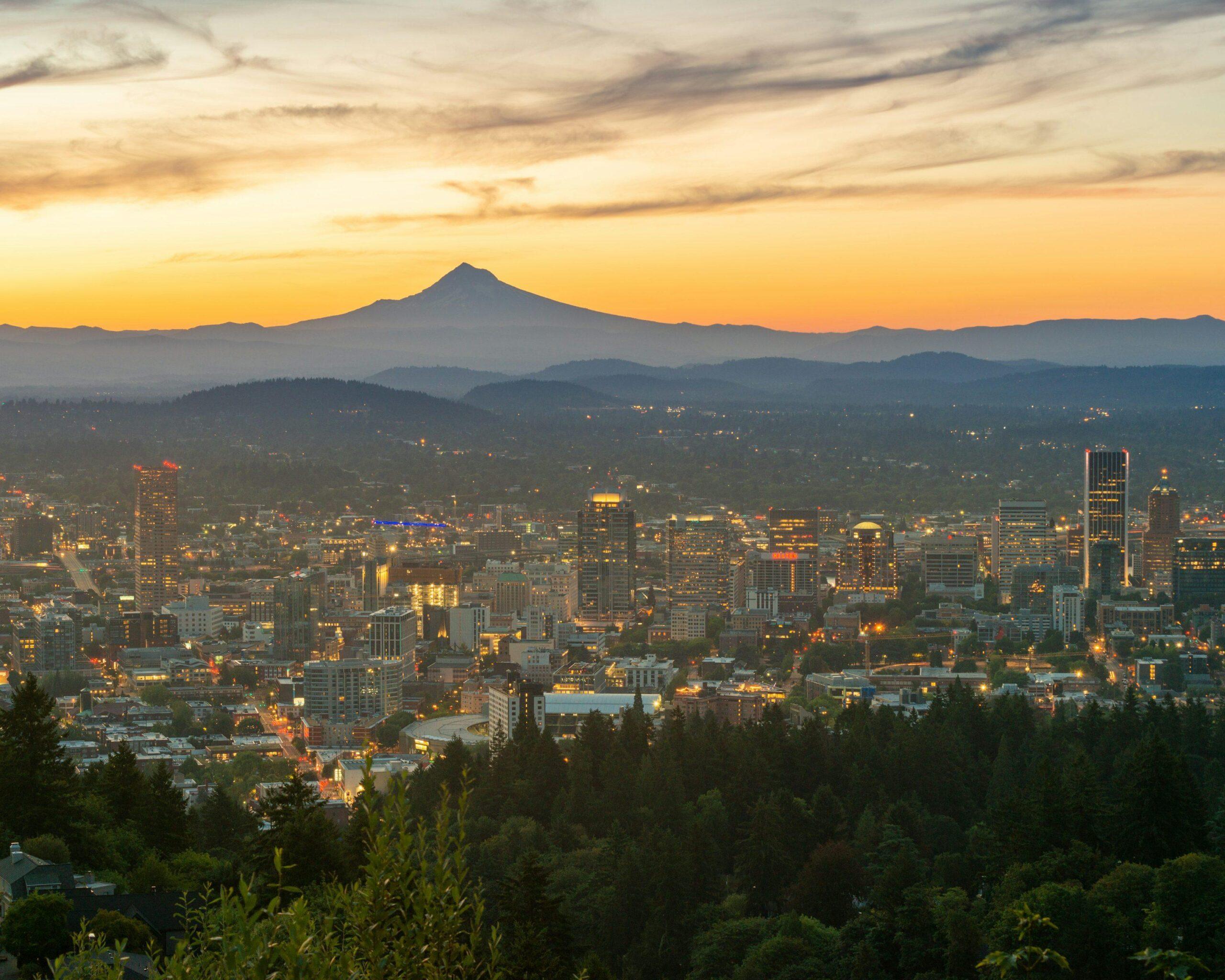 Eine beleuchtete Stadt in der Abenddämmerung mit einem majestätischen Berg im Hintergrund und Wäldern im Vordergrund