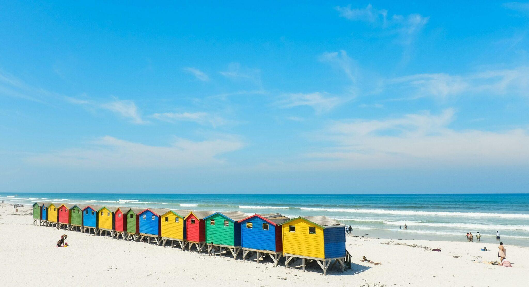 Una hilera de cabinas de playa de colores alineadas sobre la arena blanca frente al océano turquesa
