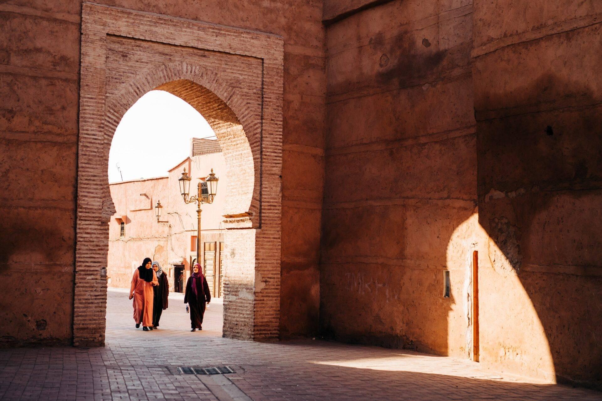 Drei Frauen durchqueren einen Backsteinbogen in einer marokkanischen Medina, die von weichem Tageslicht durchflutet wird