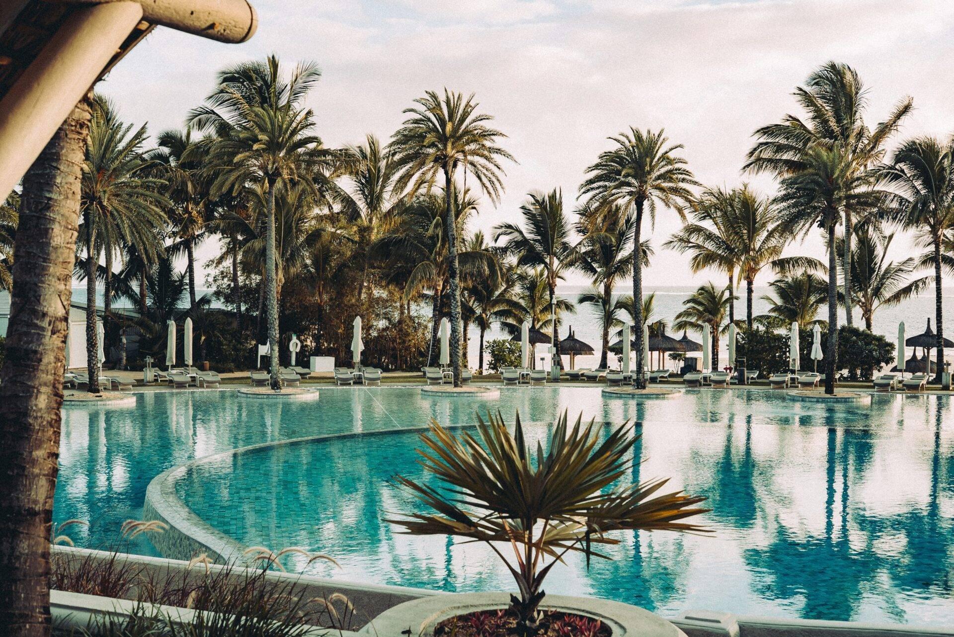 Una gran piscina turquesa bordeada de palmeras y tumbonas blancas en un lujoso resort tropical