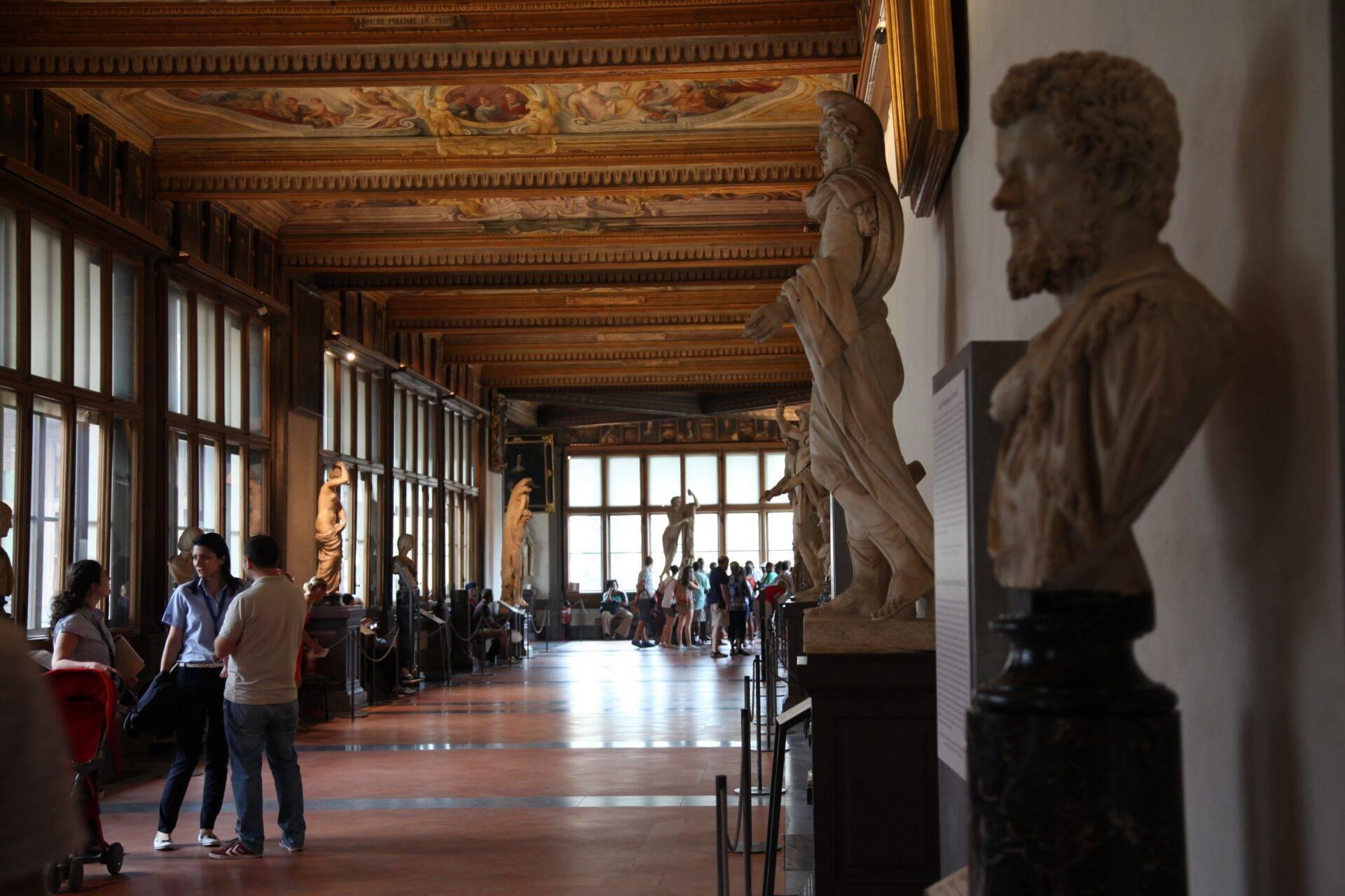 An Italian museum gallery with antique statues, an ornate painted ceiling and visitors admiring the sculptures