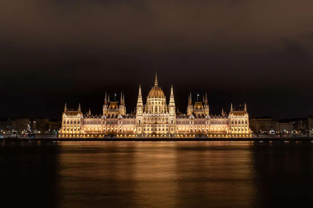 Majestuoso edificio gótico iluminado de noche a orillas de un río con reflejos dorados