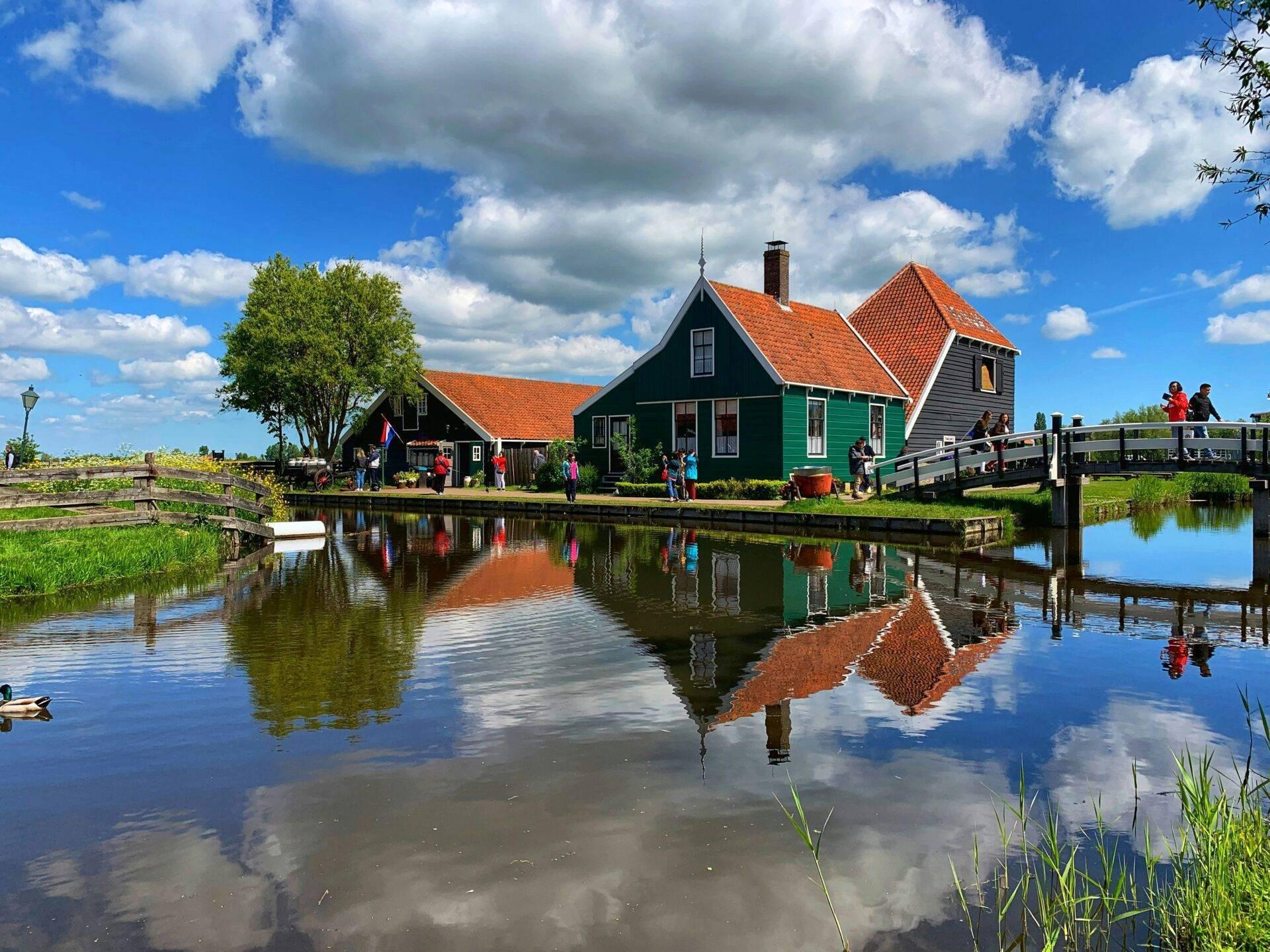 Traditionelles niederländisches Haus mit grünen Fensterläden und rotem Dach, Spiegelung im Kanal mit Besuchern und Holzbrücke