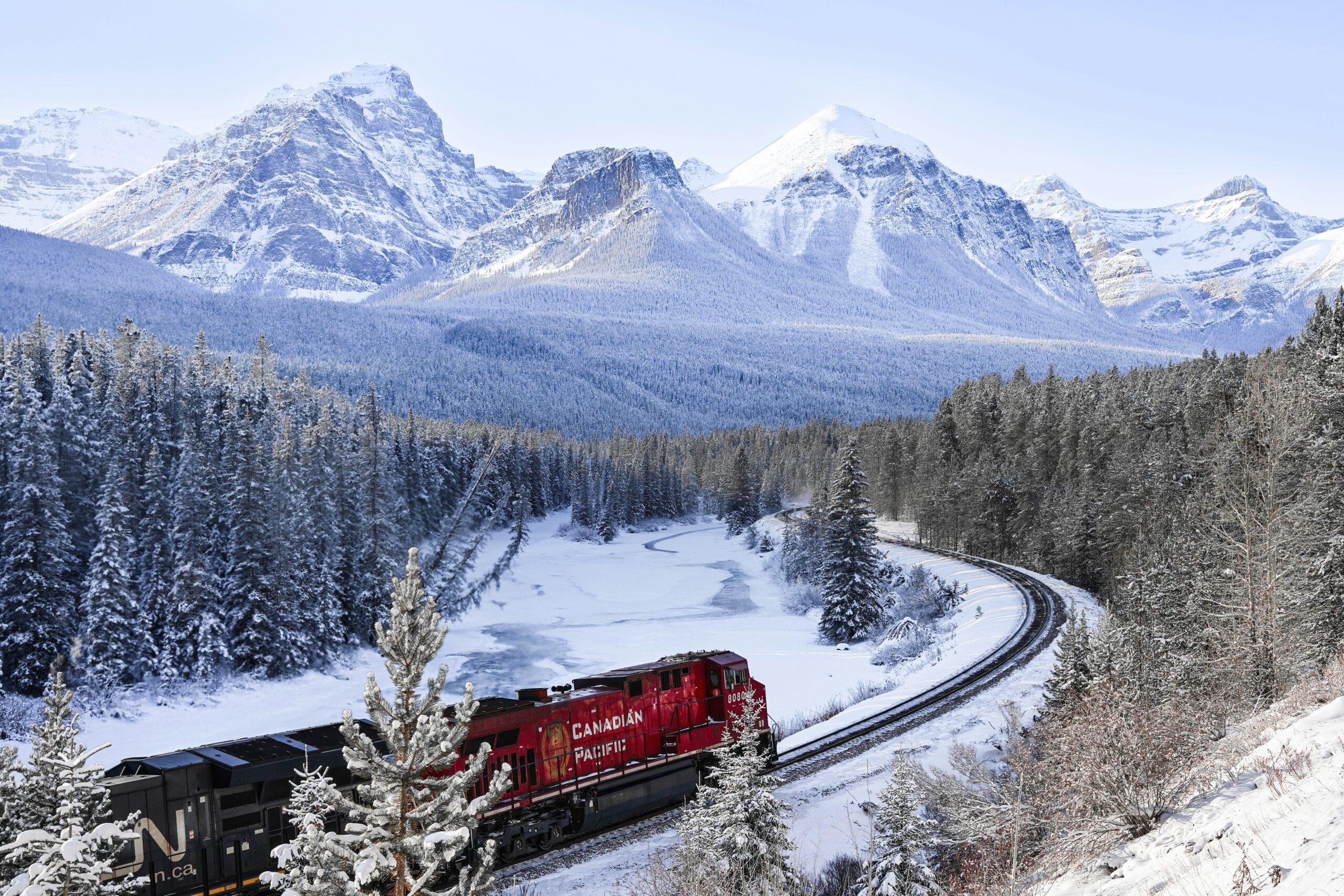 The Rocky Mountaineer crossing a forested valley in the Canadian Rockies with snow-capped peaks in the background