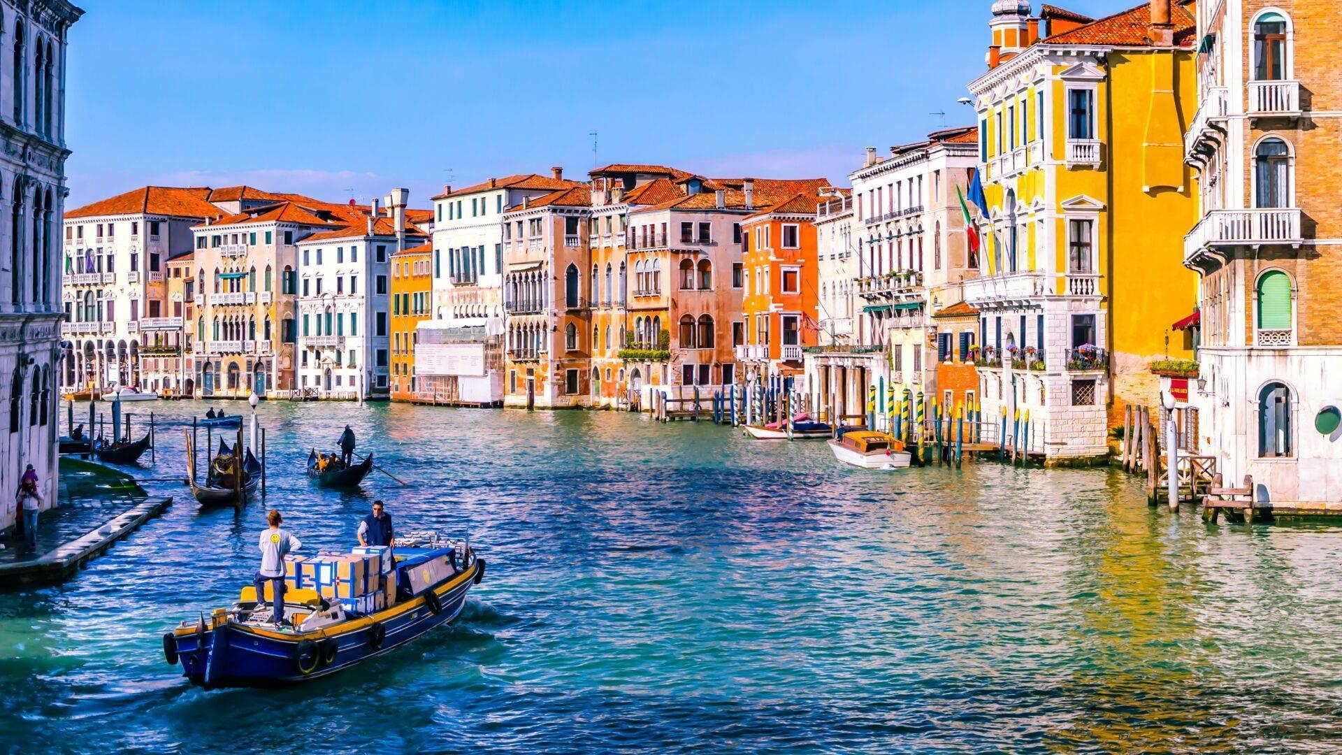 Panoramablick auf den Canal Grande mit seinen bunten Gebäuden, Gondeln und türkisfarbenem Wasser unter blauem Himmel