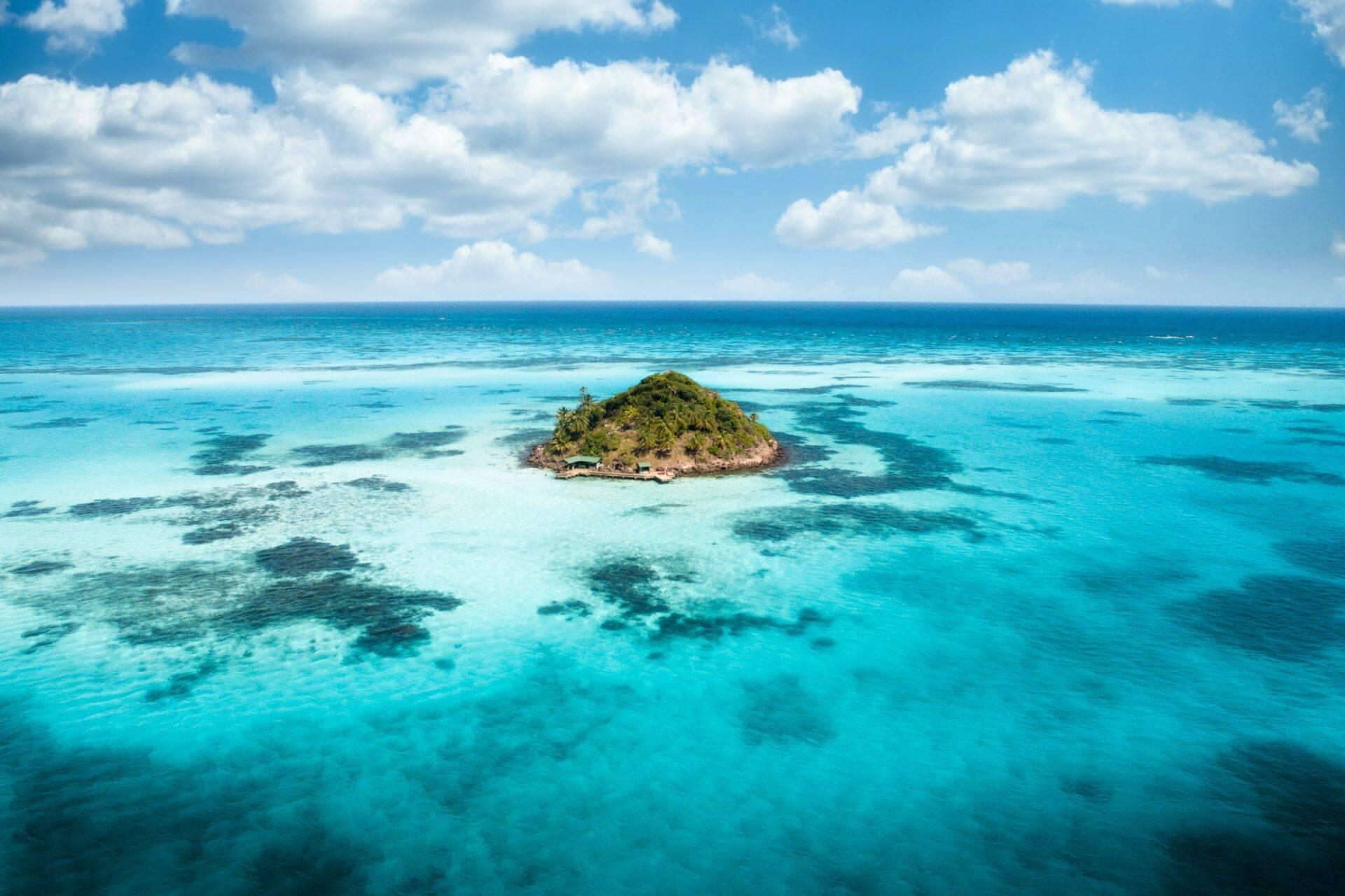 Pequeña isla tropical verde rodeada de aguas turquesas cristalinas y arrecifes de coral visibles