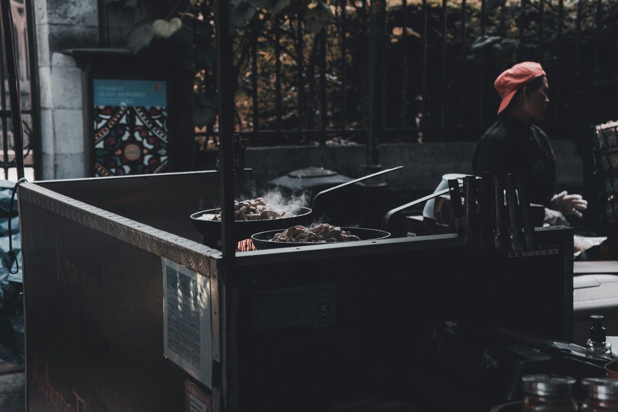 Un vendedor de street food prepara platos en woks en un callejón urbano asiático lleno de animación