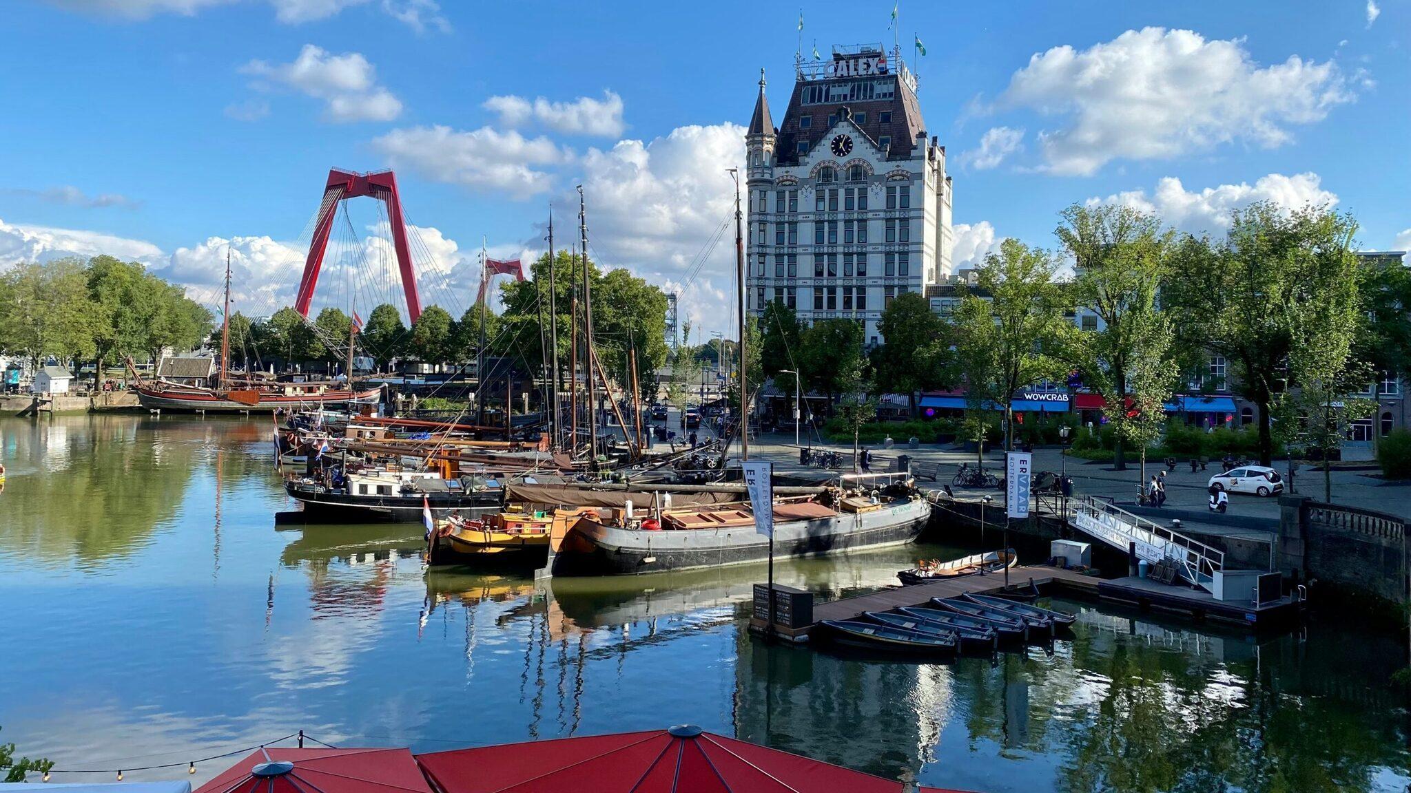 Historischer Hafen mit traditionellen Segelschiffen, roter Brücke und Uhrturm in einer europäischen Flussstadt