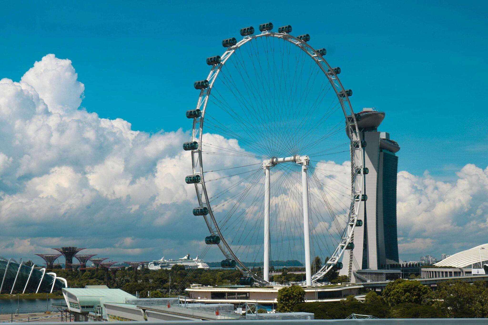 Una grande ruota panoramica futuristica bianca con cabine nere domina il paesaggio urbano sotto un cielo azzurro limpido