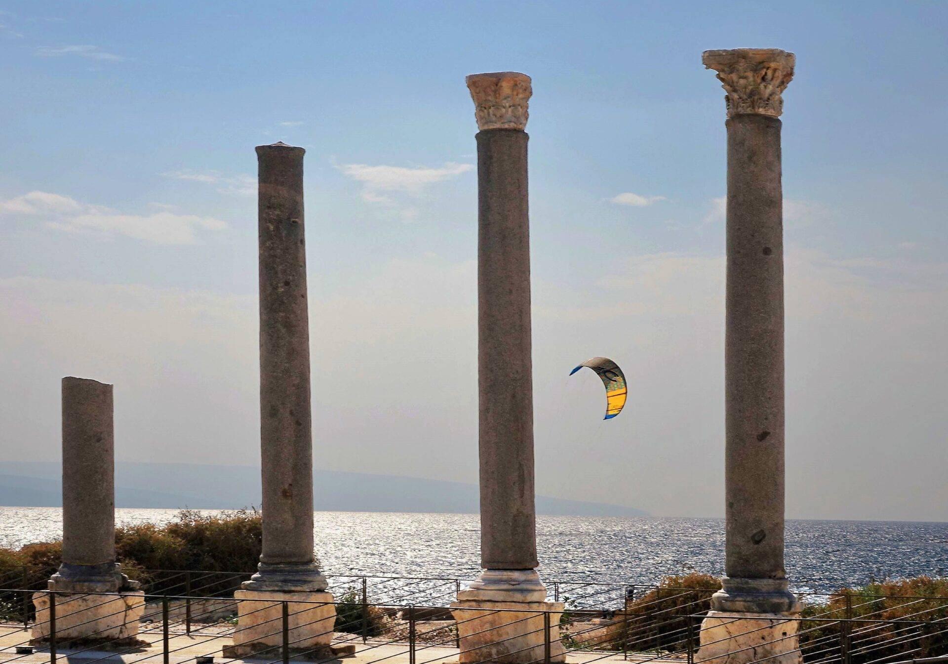 Cuatro columnas romanas antiguas frente al mar con una cometa de kitesurf al fondo