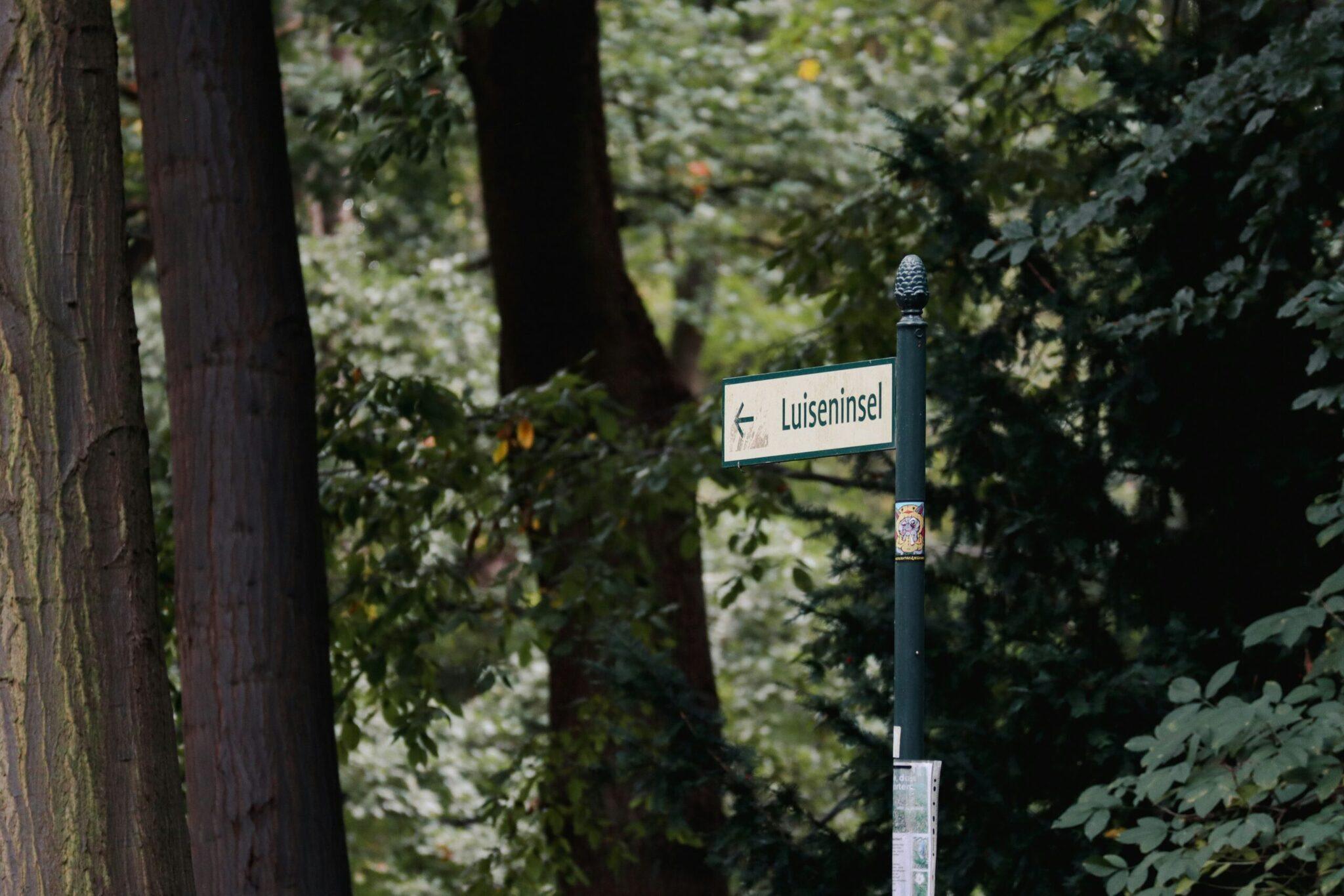 Placa de la calle «Luiseninsel» en un callejón arbolado bordeado de viejos muros de ladrillo y árboles frondosos