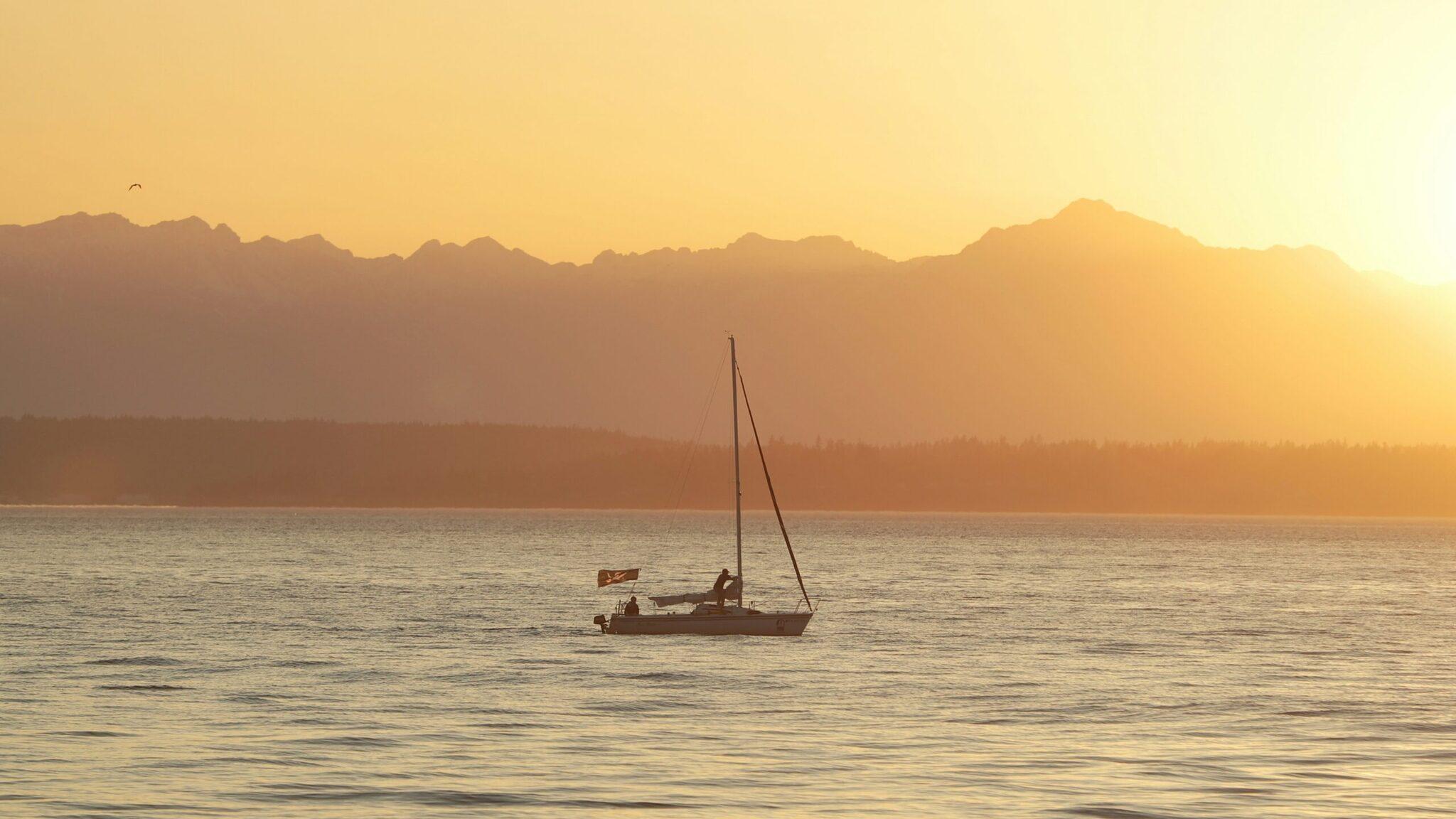 Un velero fondeado al atardecer frente a una cadena de montañas nevadas al fondo
