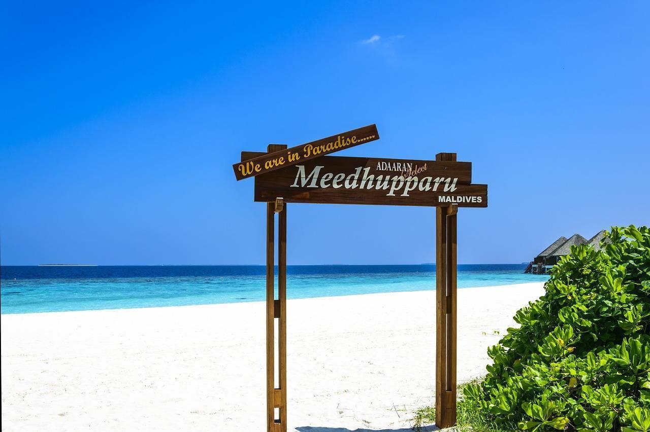 Cartello in legno “We are in Paradise” su una spiaggia di sabbia bianca con laguna turchese alle Maldive