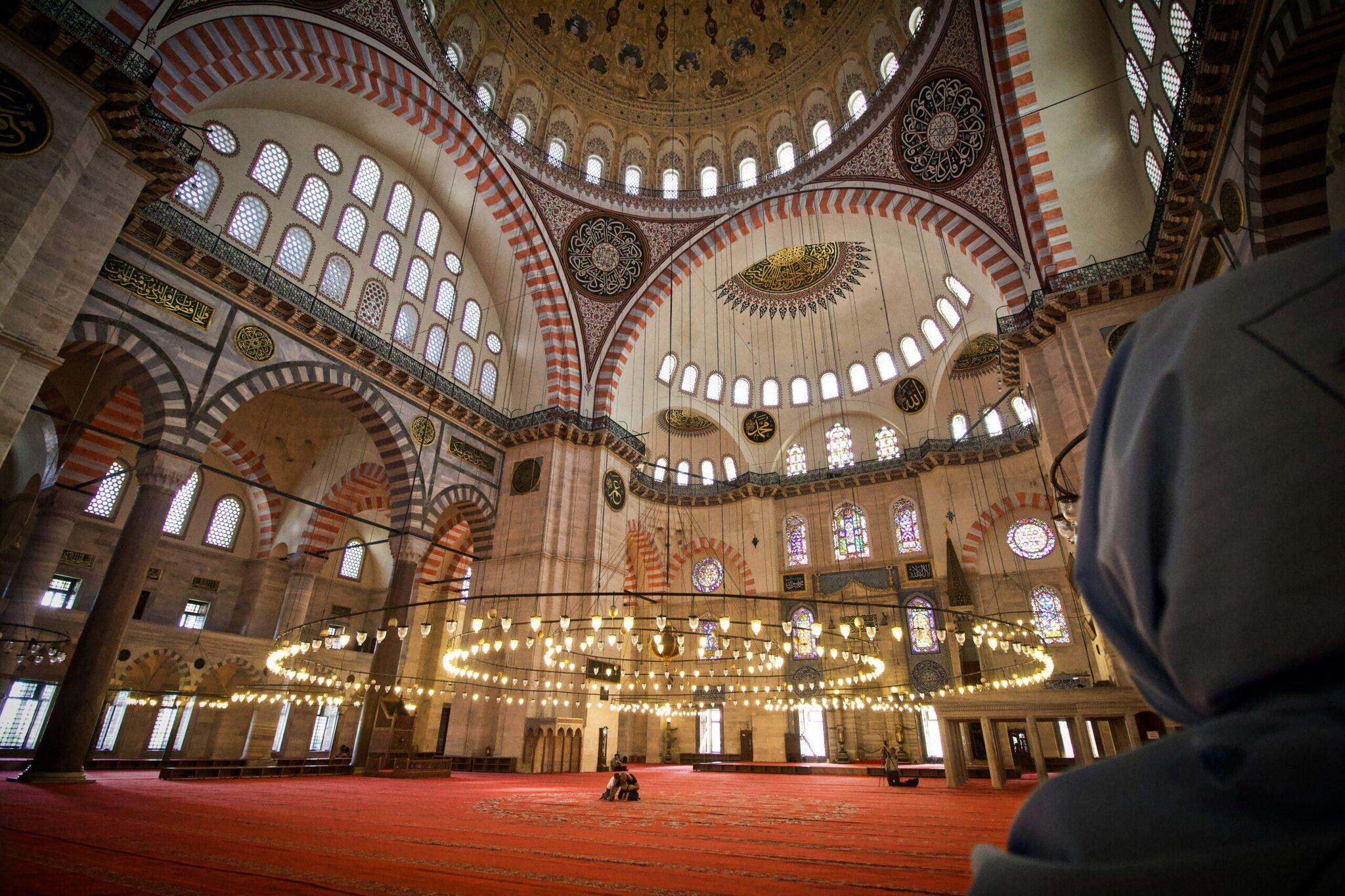 Interno maestoso di una moschea con cupola, lampadari dorati e colonne con archi rossi e bianchi