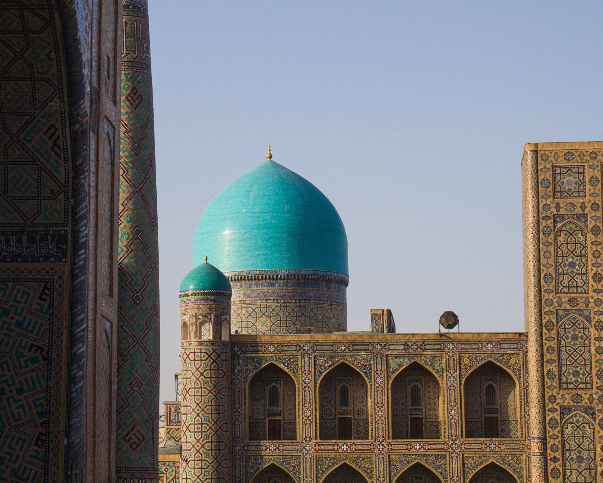 Islamisches Bauwerk mit türkis-goldenen Verzierungen, dekorierten Minaretten und hellblauer Kuppel