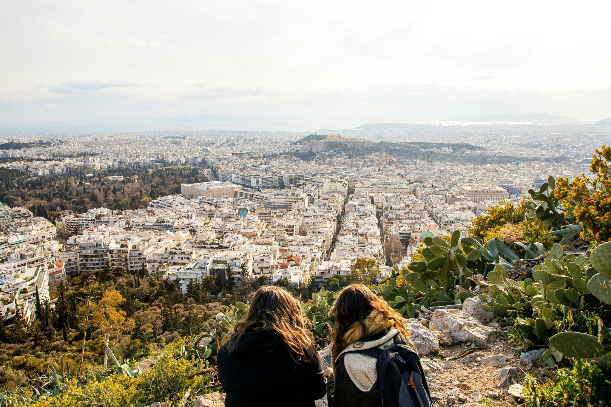 Zwei Frauen bewundern den Panoramablick auf eine mediterrane Stadt von einem Aussichtspunkt mit einheimischer Vegetation