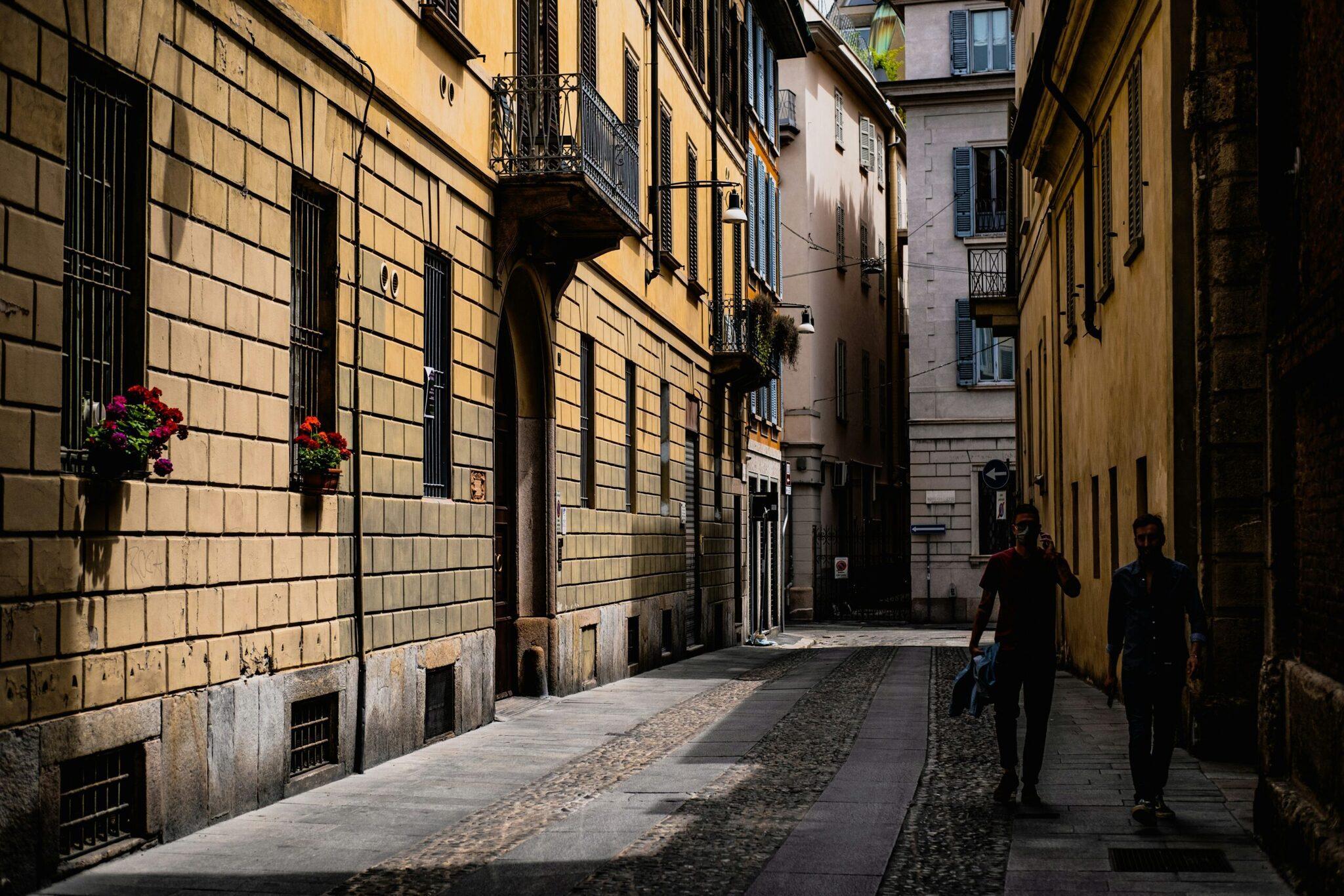 Eine enge gepflasterte Altstadtgasse einer europäischen Stadt, gesäumt von Steingebäuden in Ockerfarben mit klassischen Fassaden