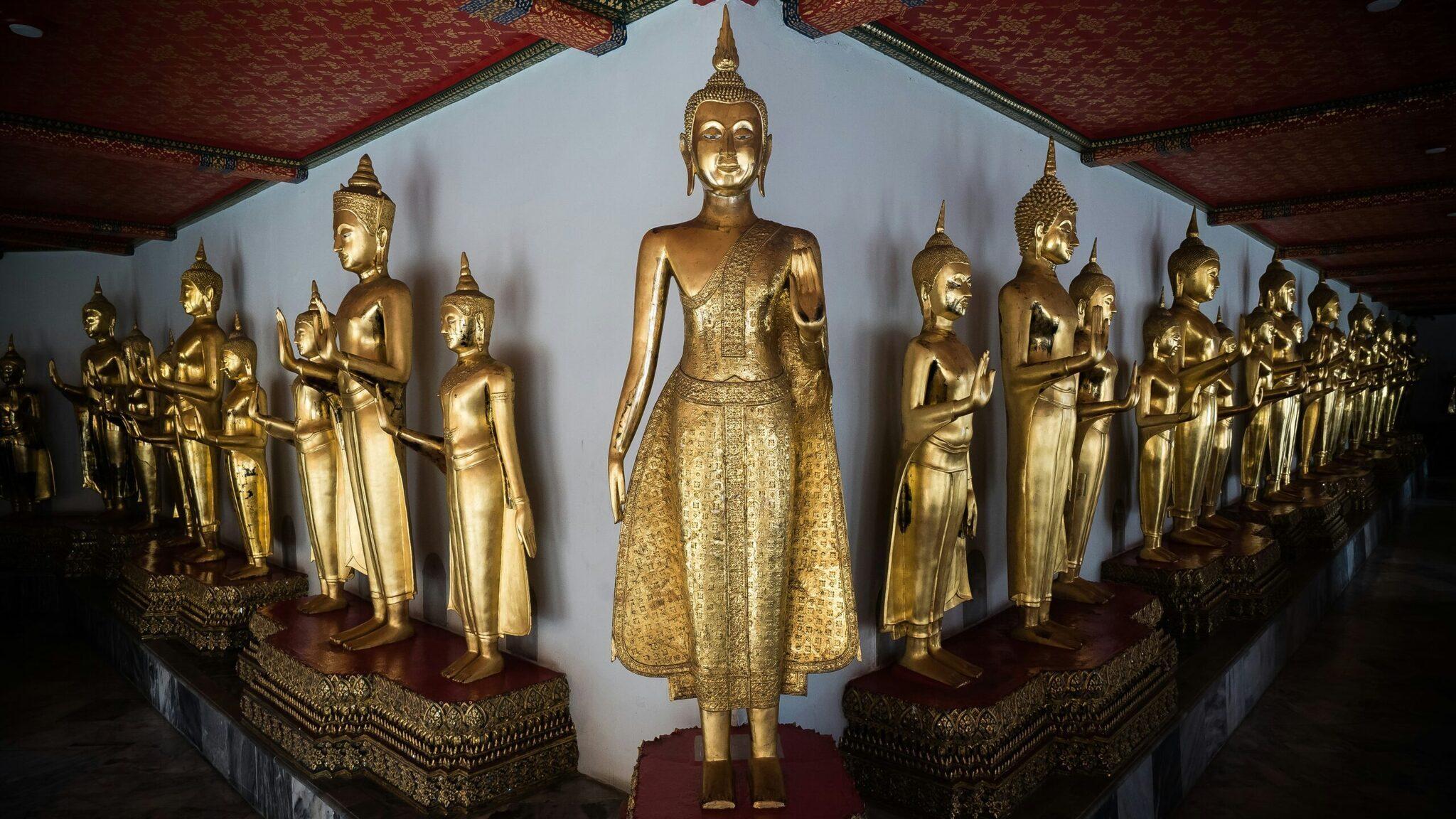 Interior gallery of a Thai temple featuring a central golden Buddha statue surrounded by rows of gilded statues