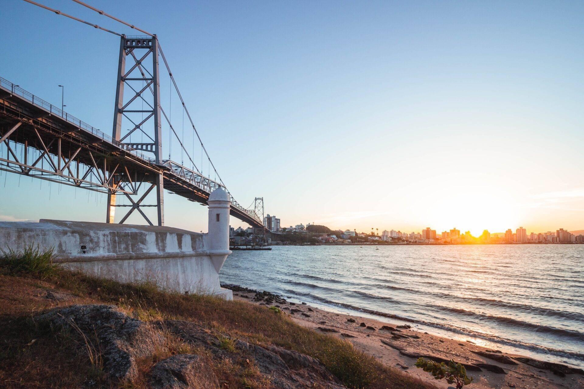 Un grande ponte sospeso in acciaio arrugginito attraversa una baia al tramonto, con una città costiera sullo sfondo