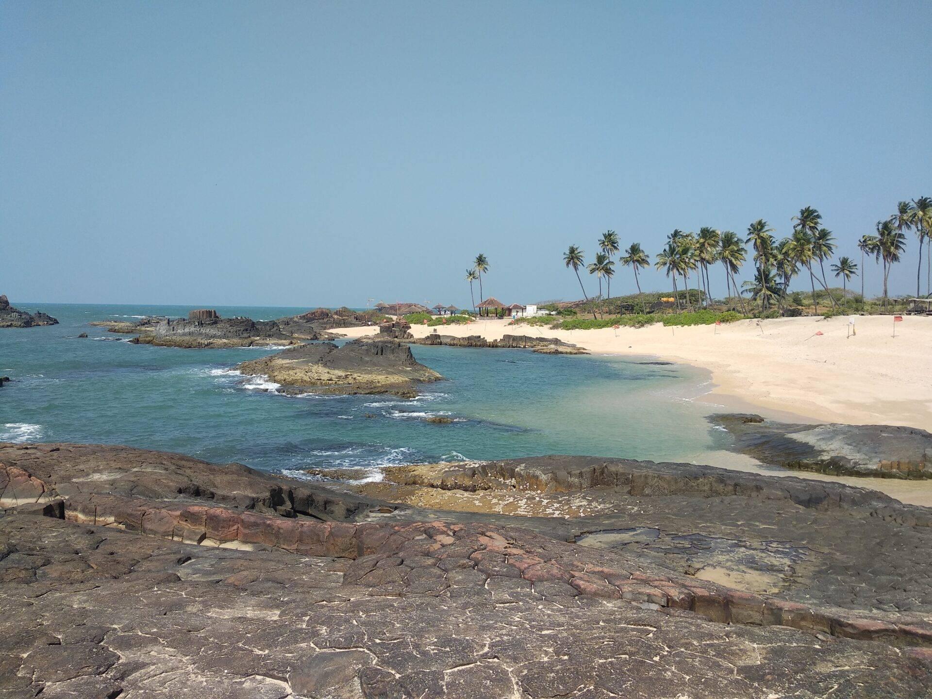 Vista costiera con spiaggia di sabbia bianca, rocce vulcaniche, palme da cocco e piccoli isolotti rocciosi in un mare turchese
