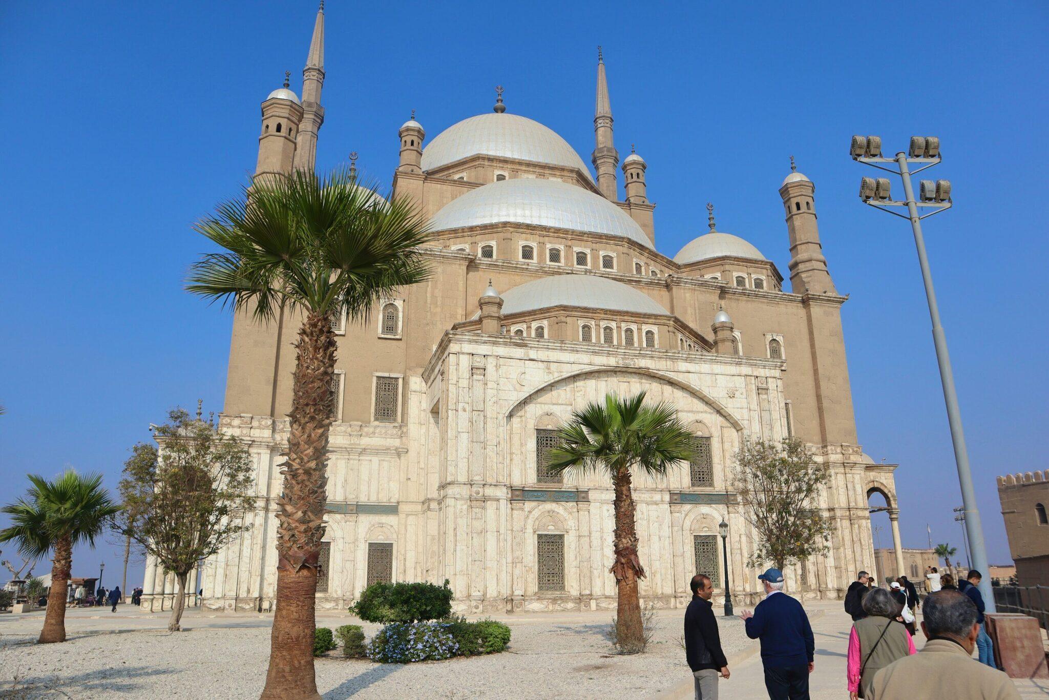 Mezquita blanca de cúpula imponente con minaretes, rodeada de palmeras, bajo un cielo despejado