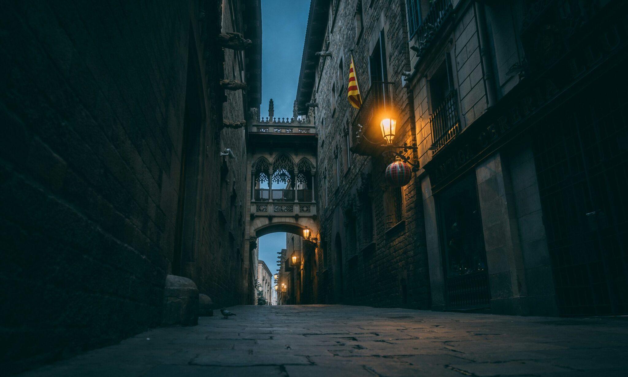 Callejuelas góticas estrechas del barrio antiguo de Barcelona al atardecer, con farola y bandera catalana