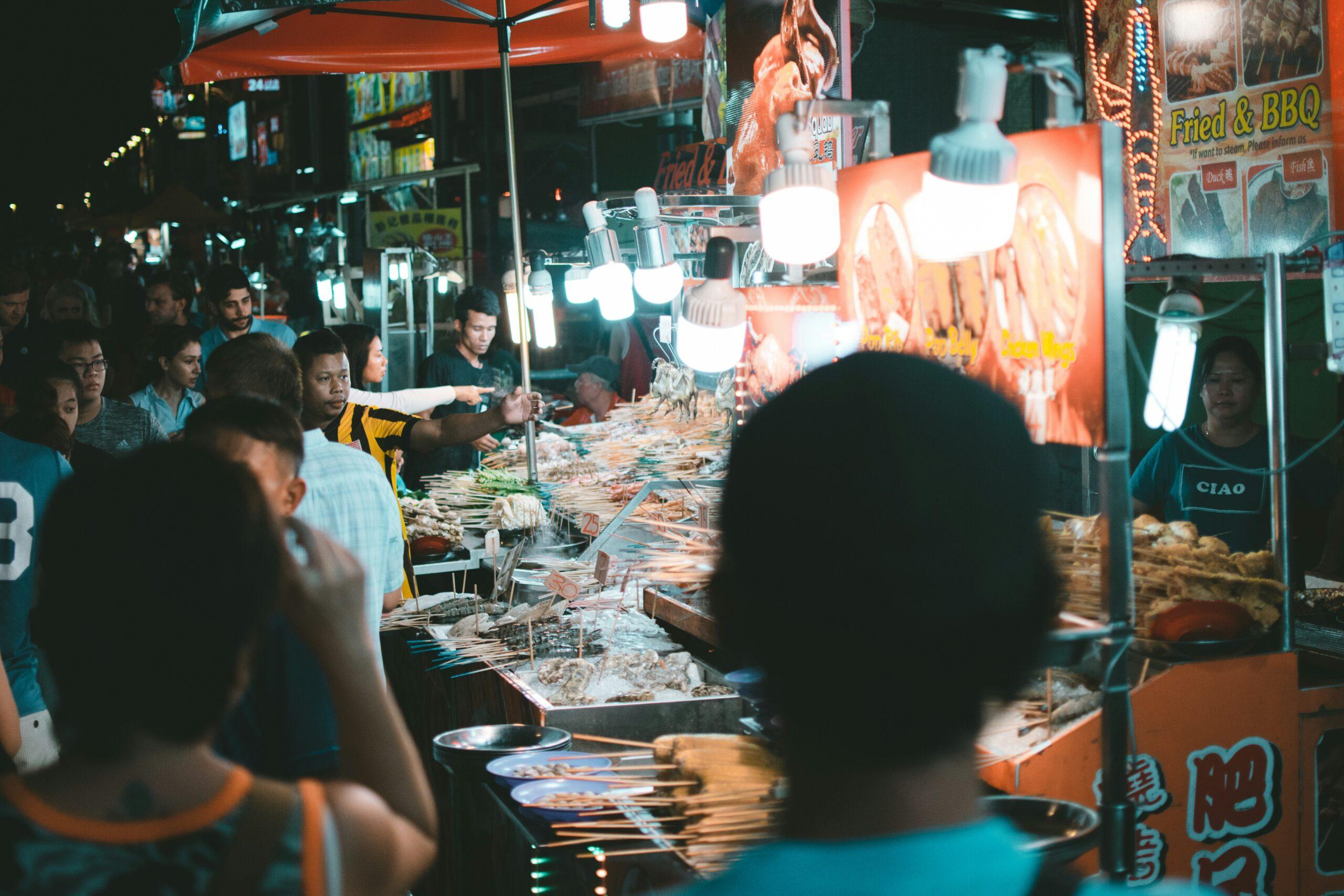 Belebter nächtlicher Straßenmarkt mit Grillständen, umgeben von Besuchern unter warmen Lichtern