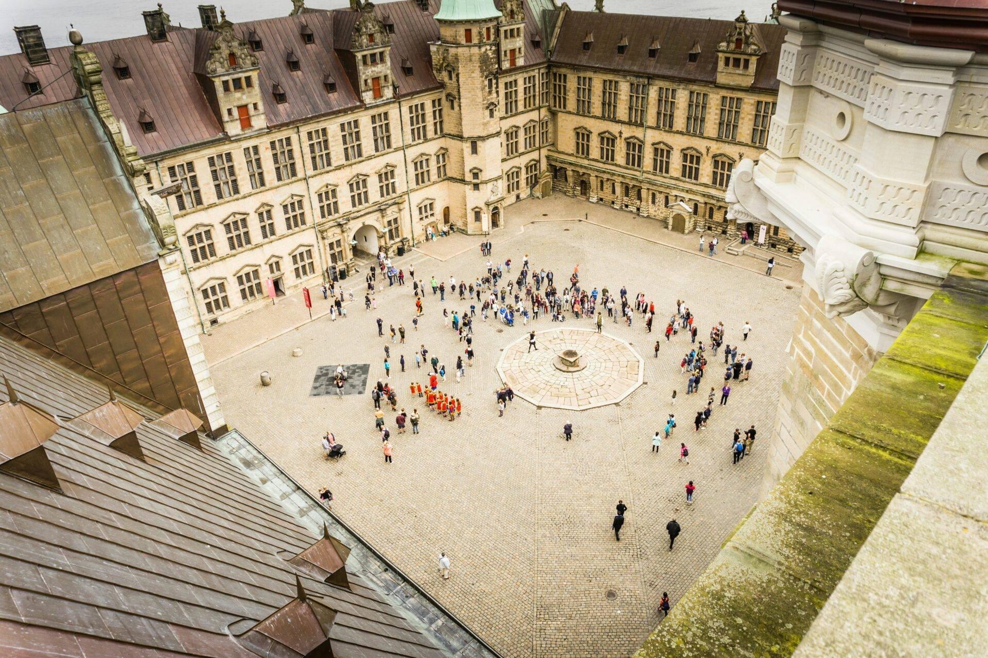 Vista aerea di un cortile interno di castello medievale con turisti, edifici in pietra e tetti in rame