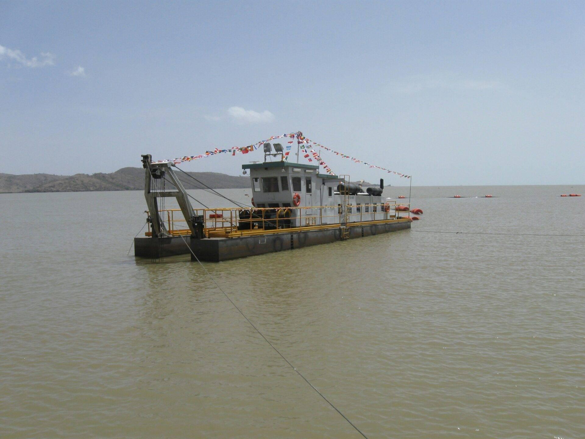 A white and yellow passenger ferry moored in a calm bay, decorated with colourful flags, with mountains in the background