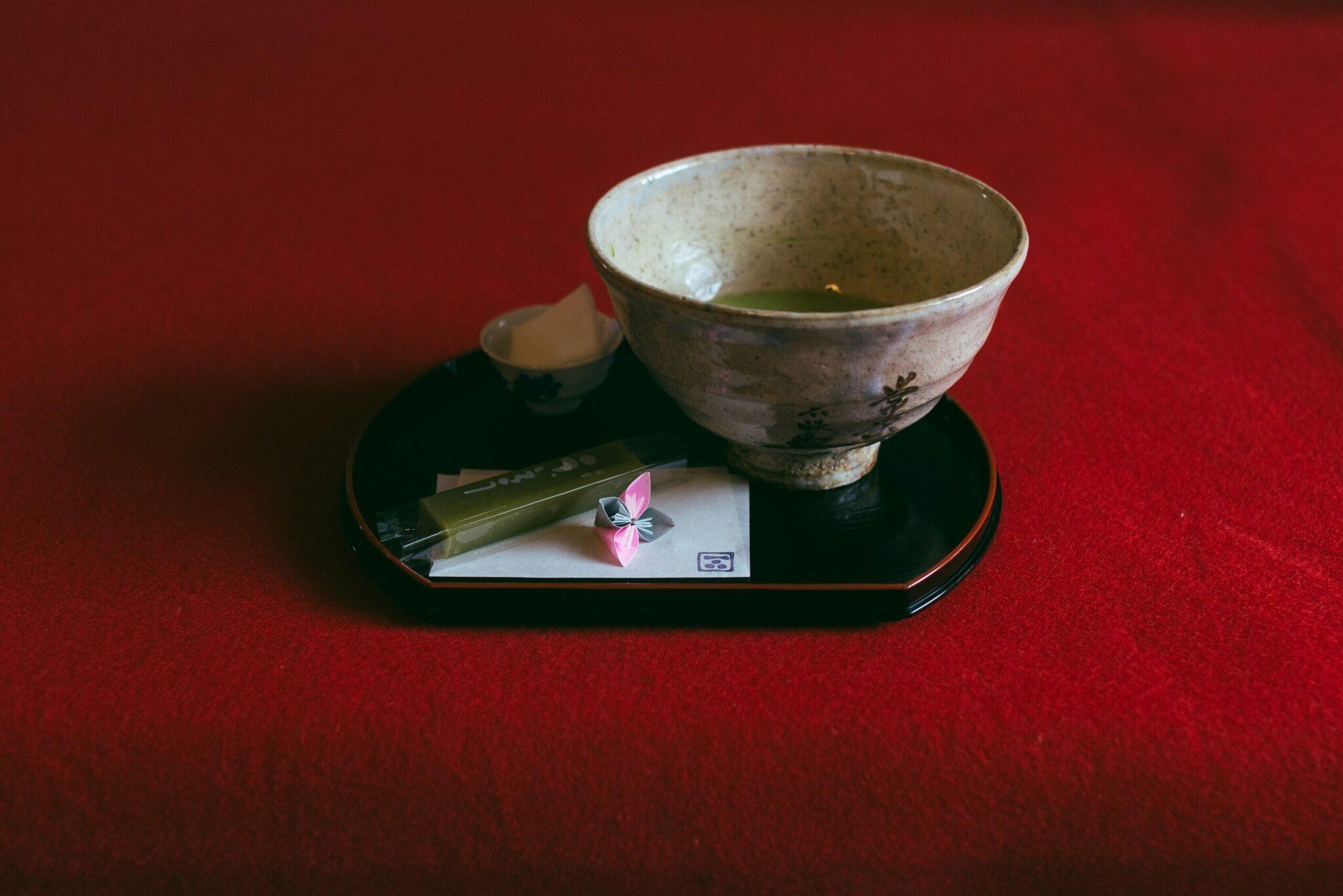 Un cuenco de té matcha tradicional presentado en una bandeja negra con accesorios de ceremonia del té japonesa