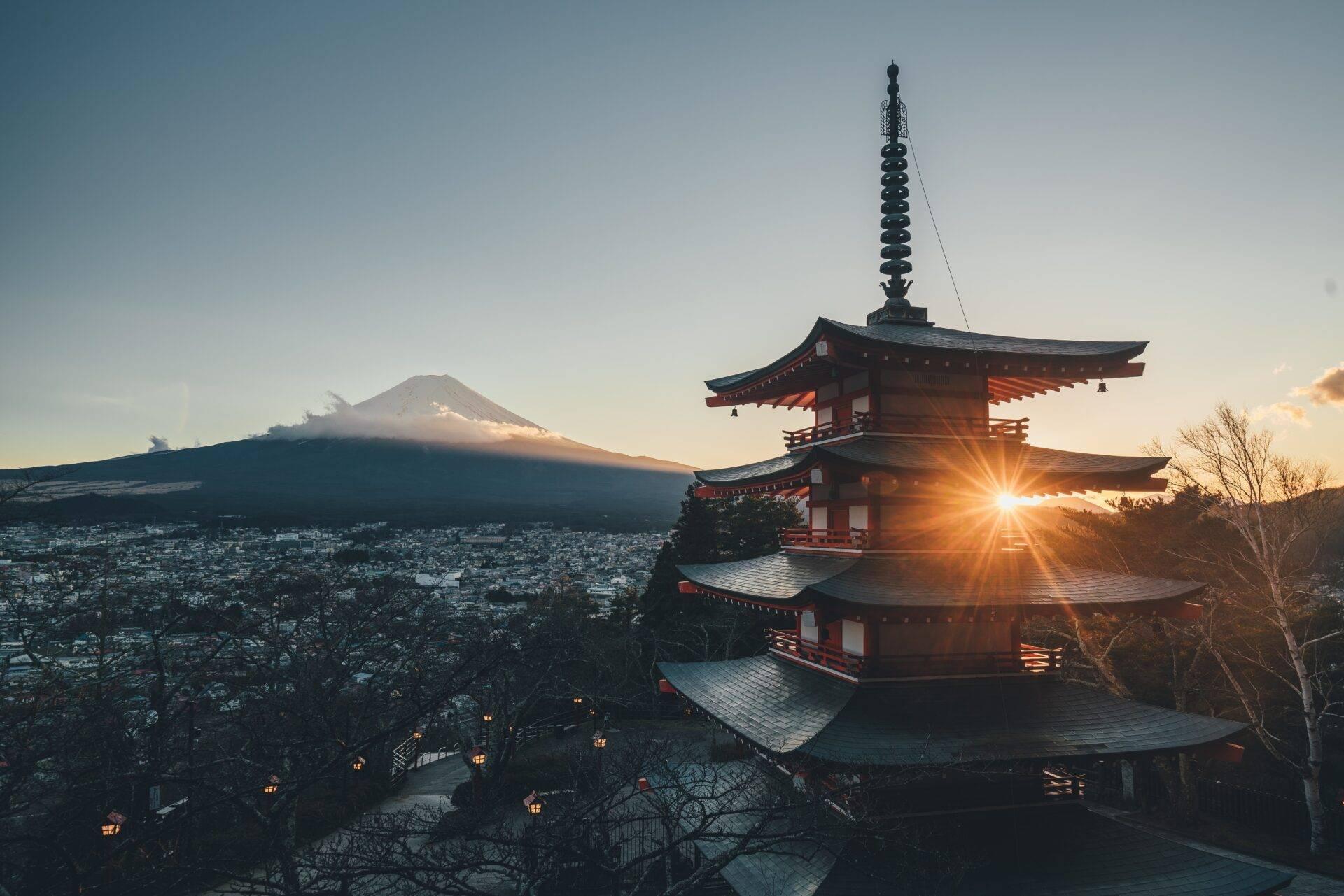 Un templo budista tradicional al atardecer con el Monte Fuji nevado al fondo y una ciudad iluminada