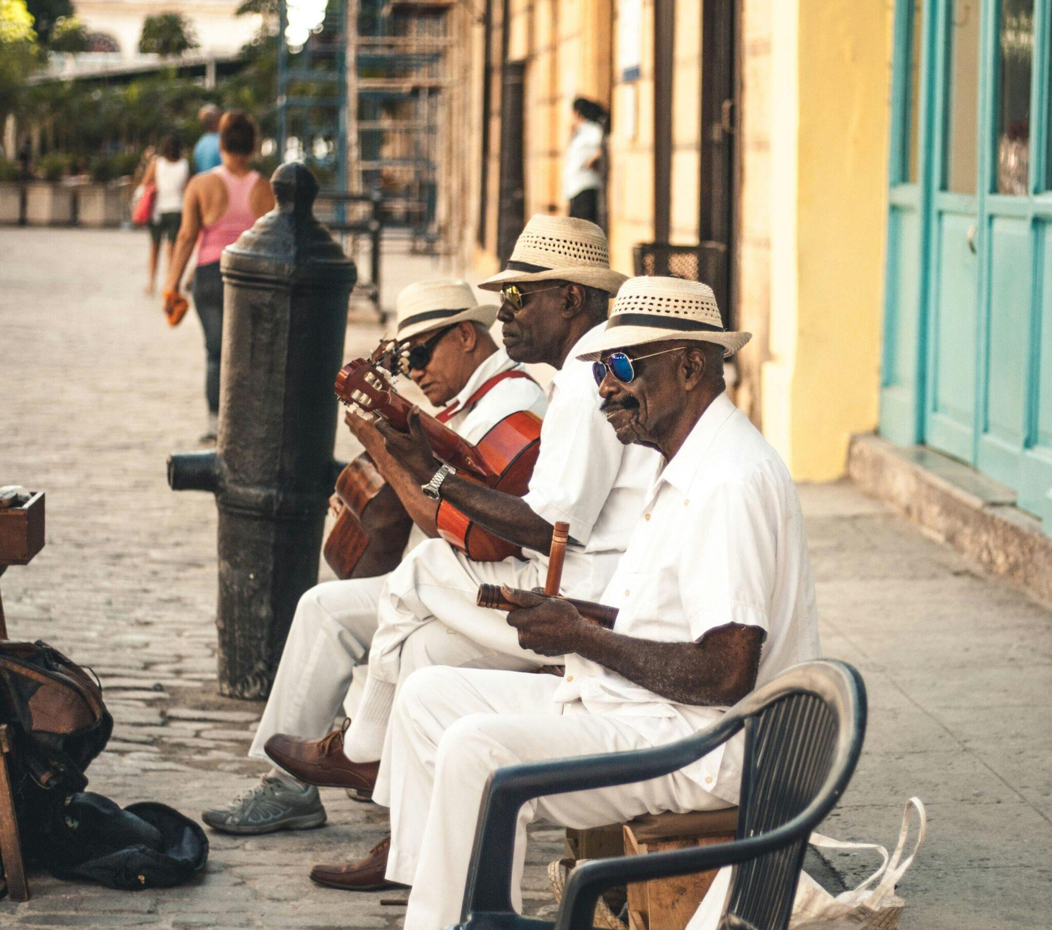 Tres músicos tocan la guitarra en una calle adoquinada colonial con fachadas de colores amarillo y turquesa