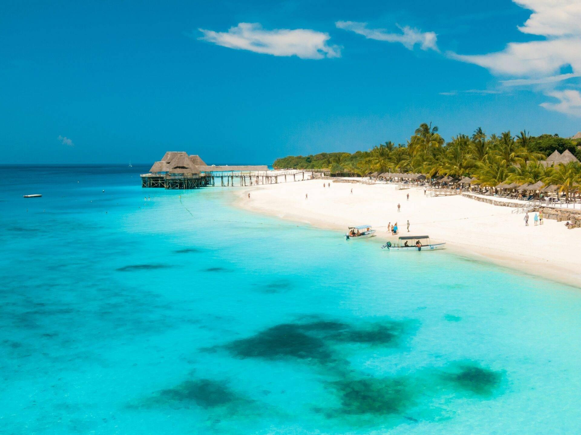 Spiaggia tropicale con laguna turchese, bungalow su palafitte, palme e sabbia bianca sotto un cielo azzurro