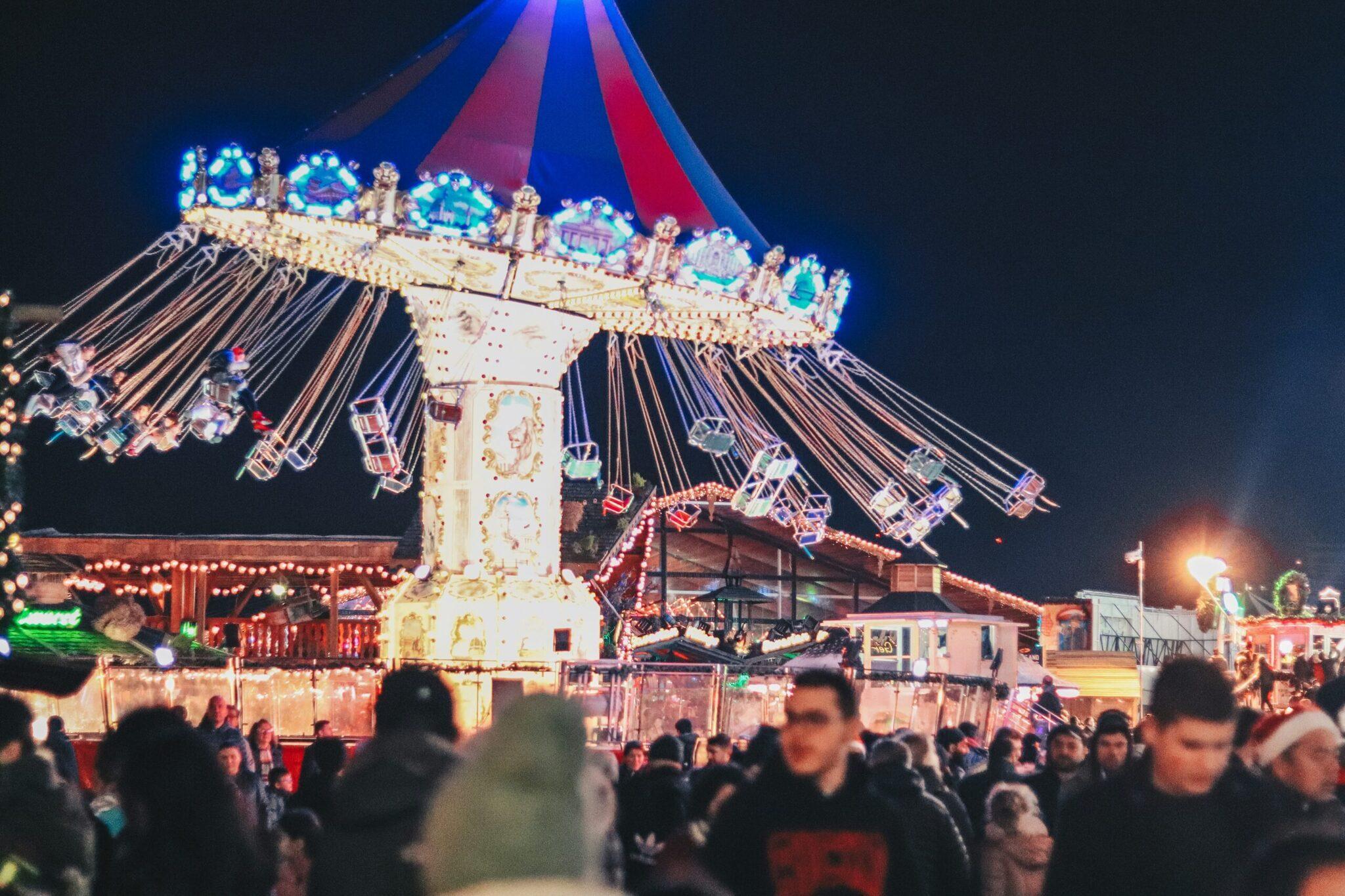 Atracción iluminada de noche en un mercado navideño con multitud de visitantes y decoración festiva de colores