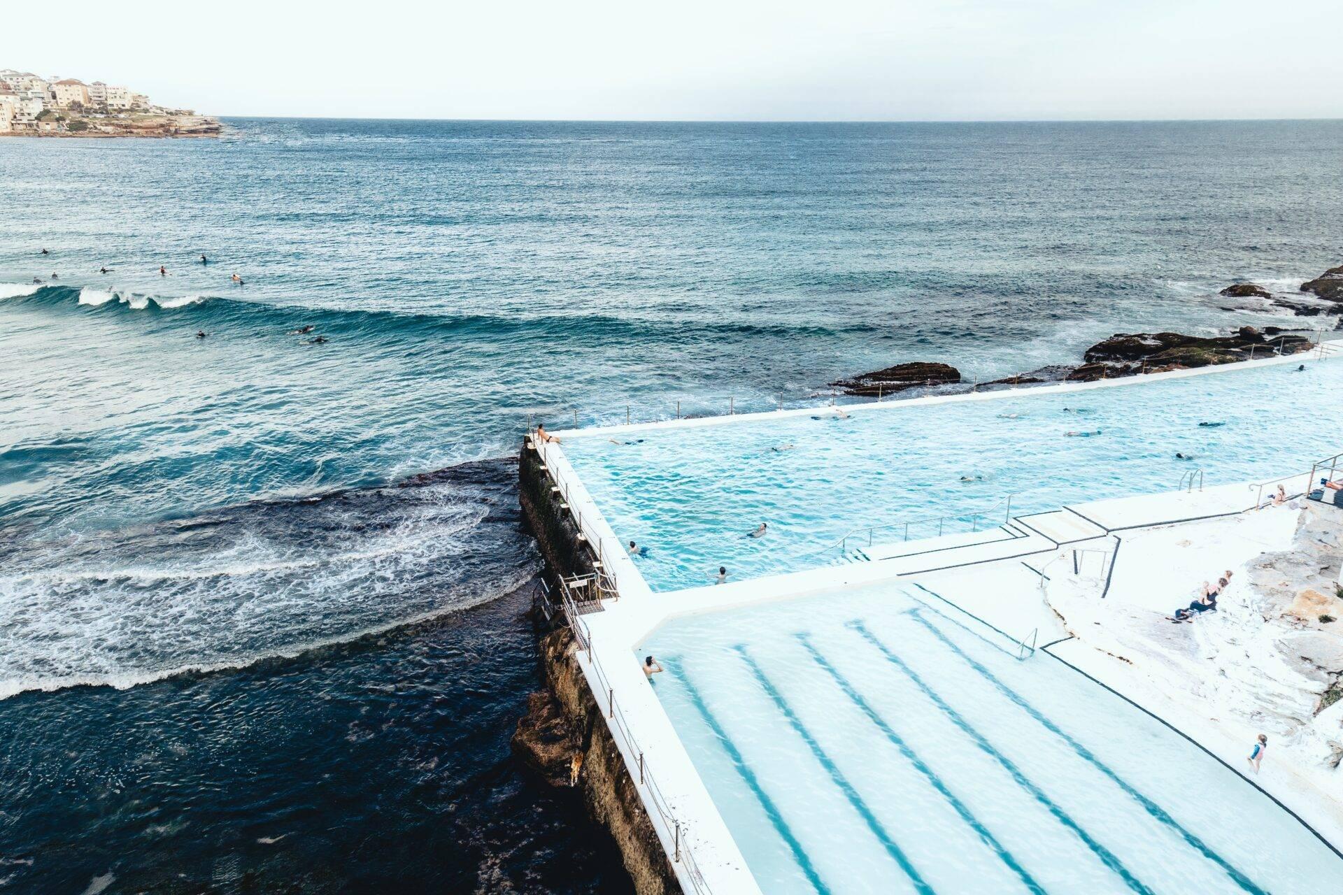 Piscina olimpica sul bordo del mare con vista sull’oceano turchese e costa rocciosa sotto un cielo sgombro