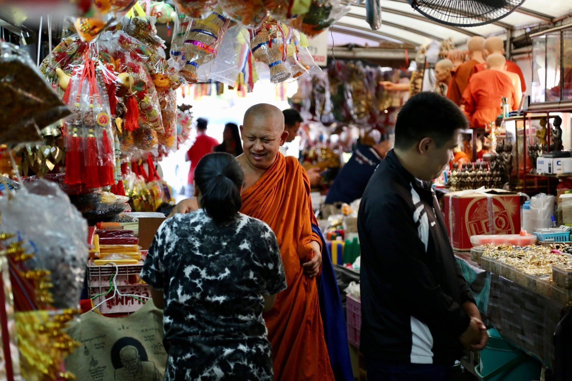 Un monaco buddista in veste arancione in un mercato coperto pieno di decorazioni religiose colorate e statuette
