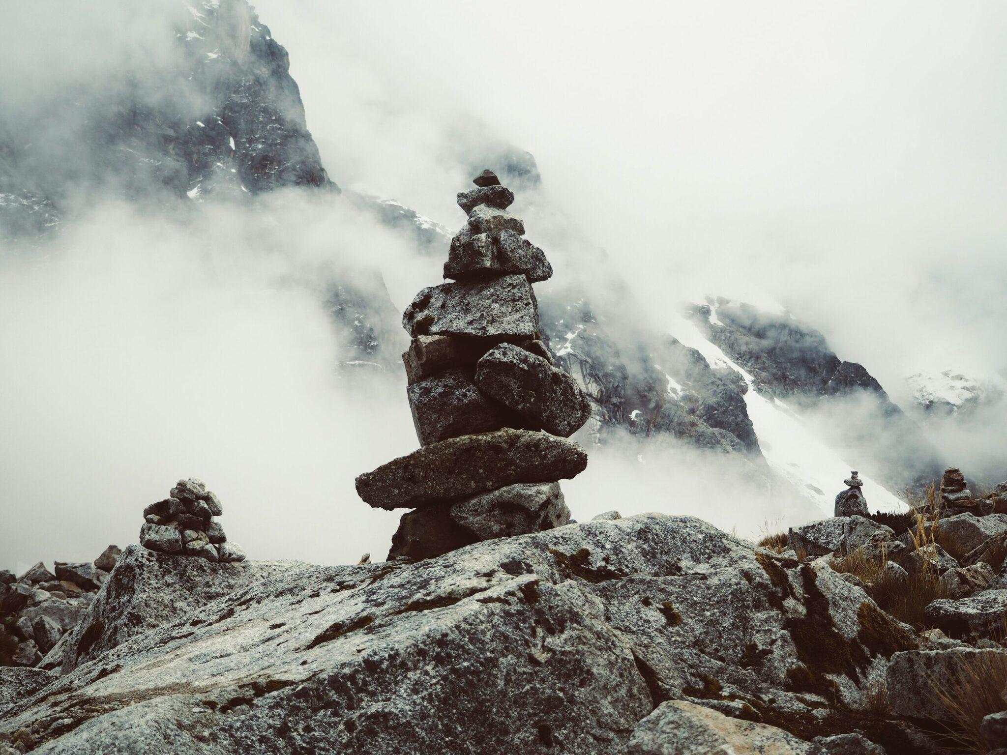 Stone cairns stacked in misty mountain scenery with snow-capped rocky peaks in the background