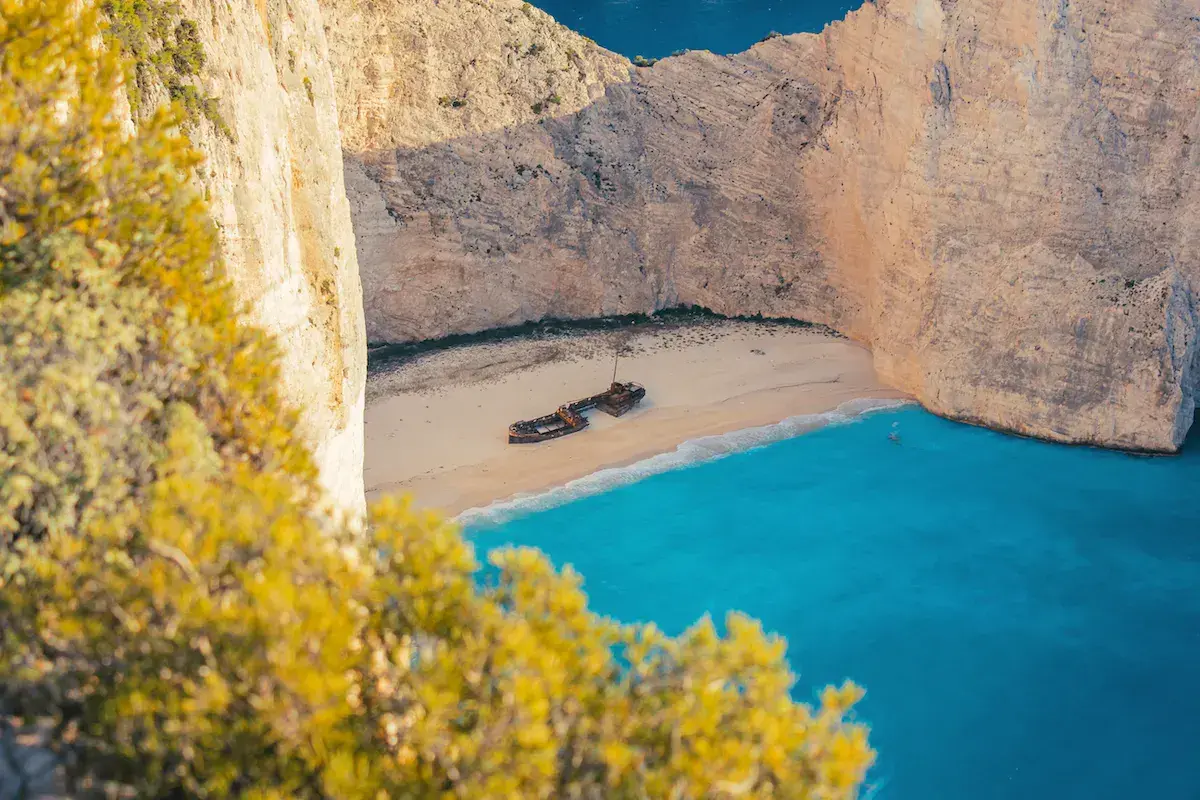 Vista aérea de una bahía encajonada con acantilados blancos, playa de arena, agua turquesa y el naufragio de un barco encallado