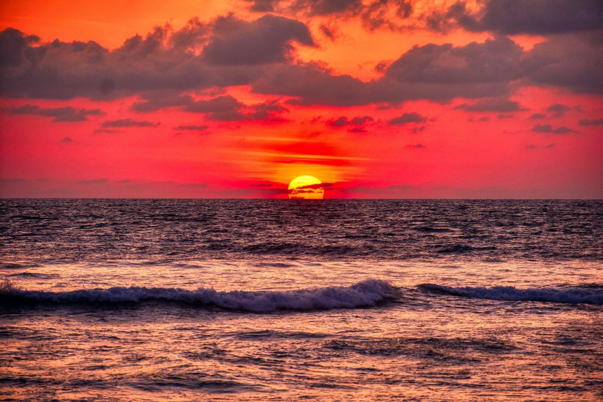 Flammenroter Sonnenuntergang über dem Ozean mit Wellen und spektakulär orangerot leuchtendem Himmel