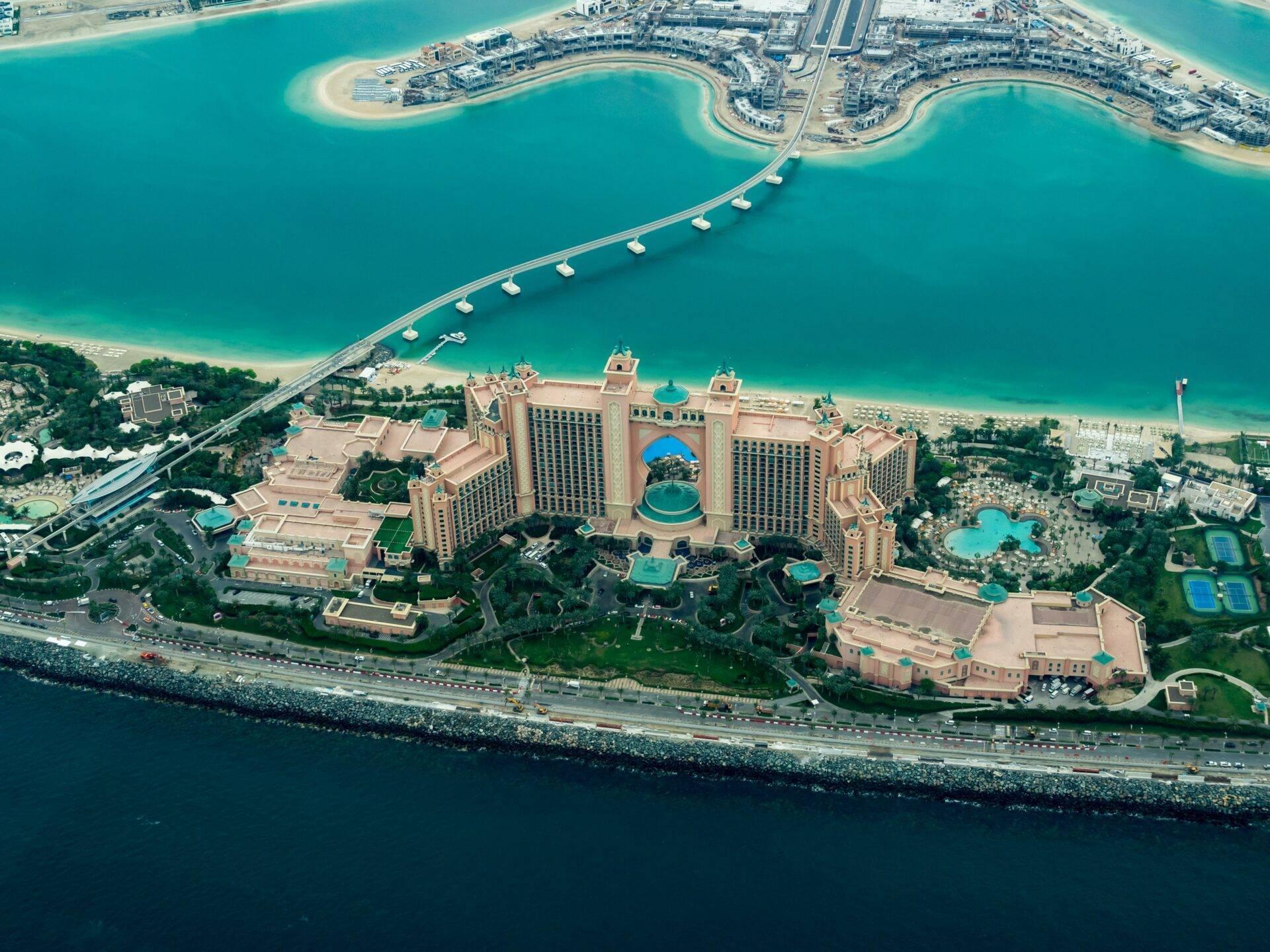 Luftaufnahme eines luxuriösen Strandresorts mit goldener Architektur, türkisblauen Pools und Privatstrand in den Arabischen Emiraten